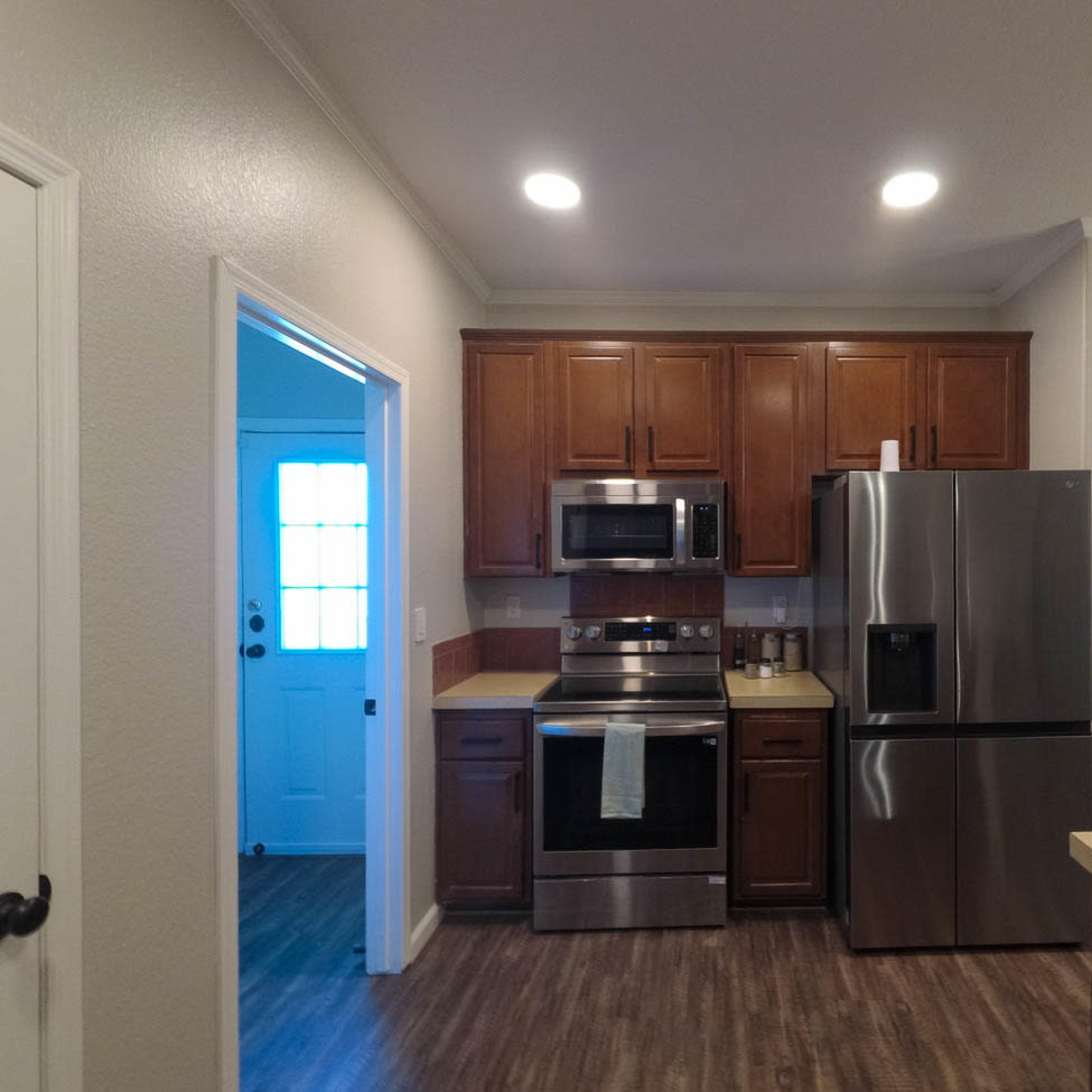 A modern kitchen featuring wooden cabinets, stainless steel appliances, and a doorway leading to a blue front entrance.