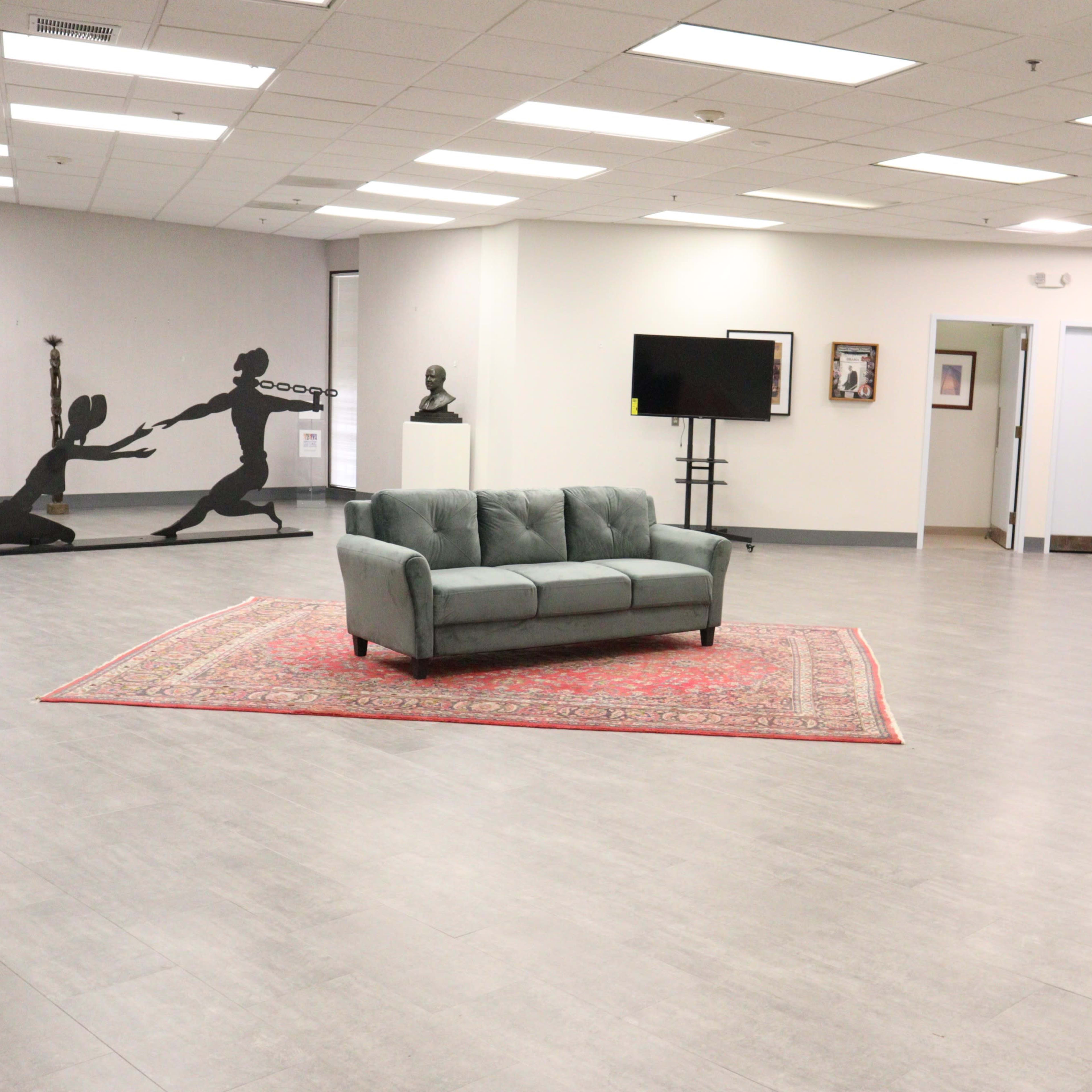 A spacious room with a gray couch on a red area rug, accompanied by artwork on the walls and a large black silhouette sculpture in the corner.