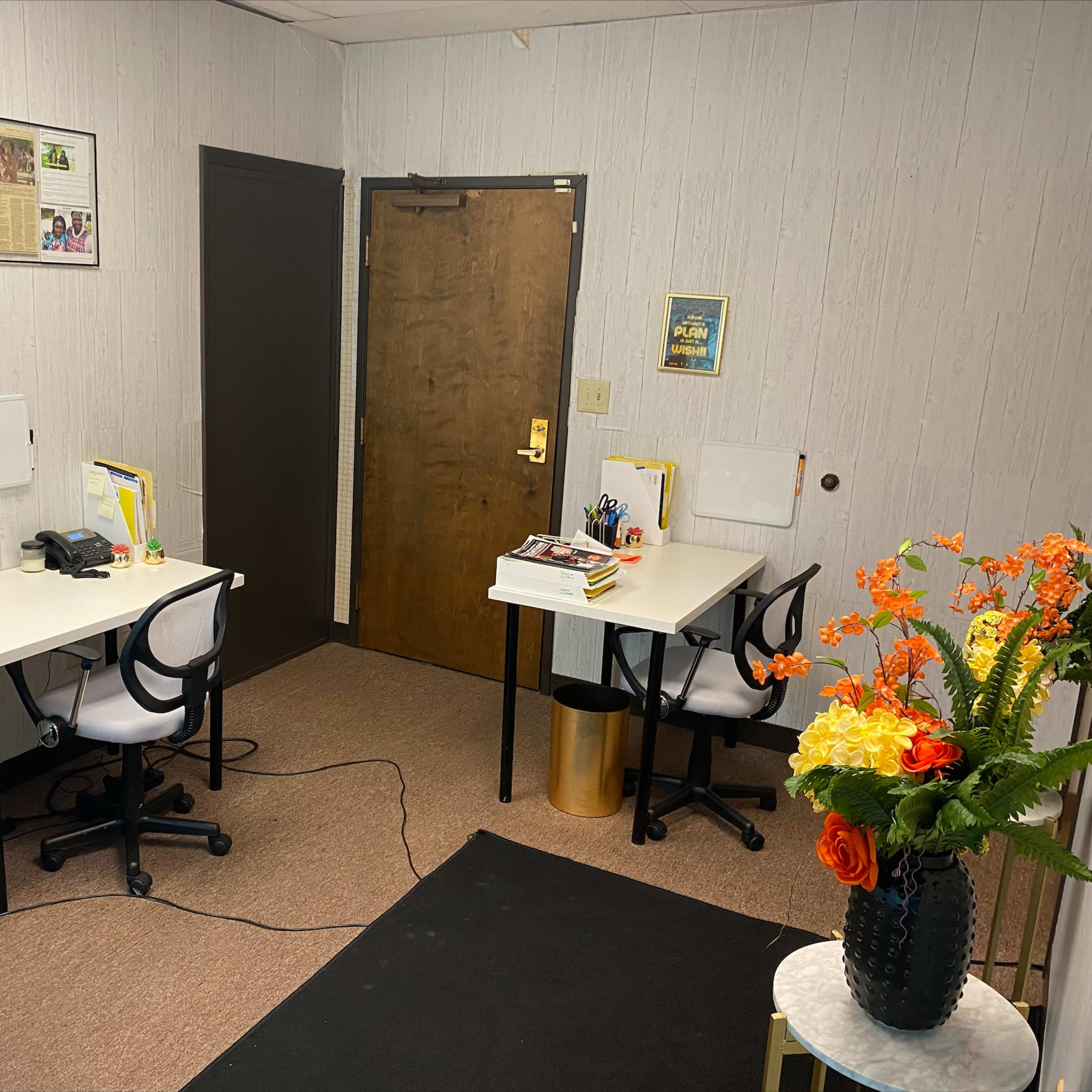 A small office space featuring two desks with chairs, a phone, office supplies, and a door leading outside.