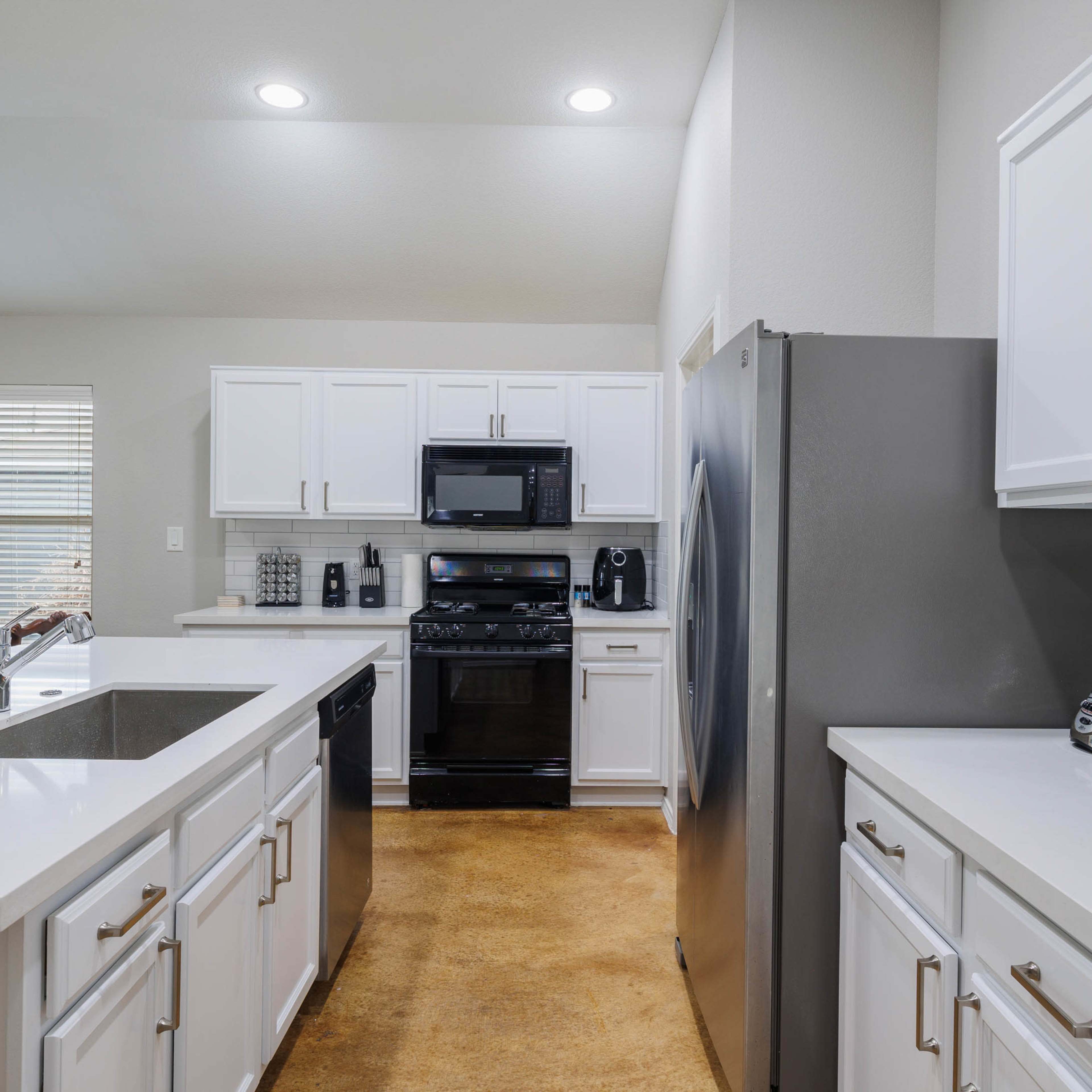 The kitchen features white cabinetry, a stainless steel refrigerator, and black appliances integrated with a spacious layout.