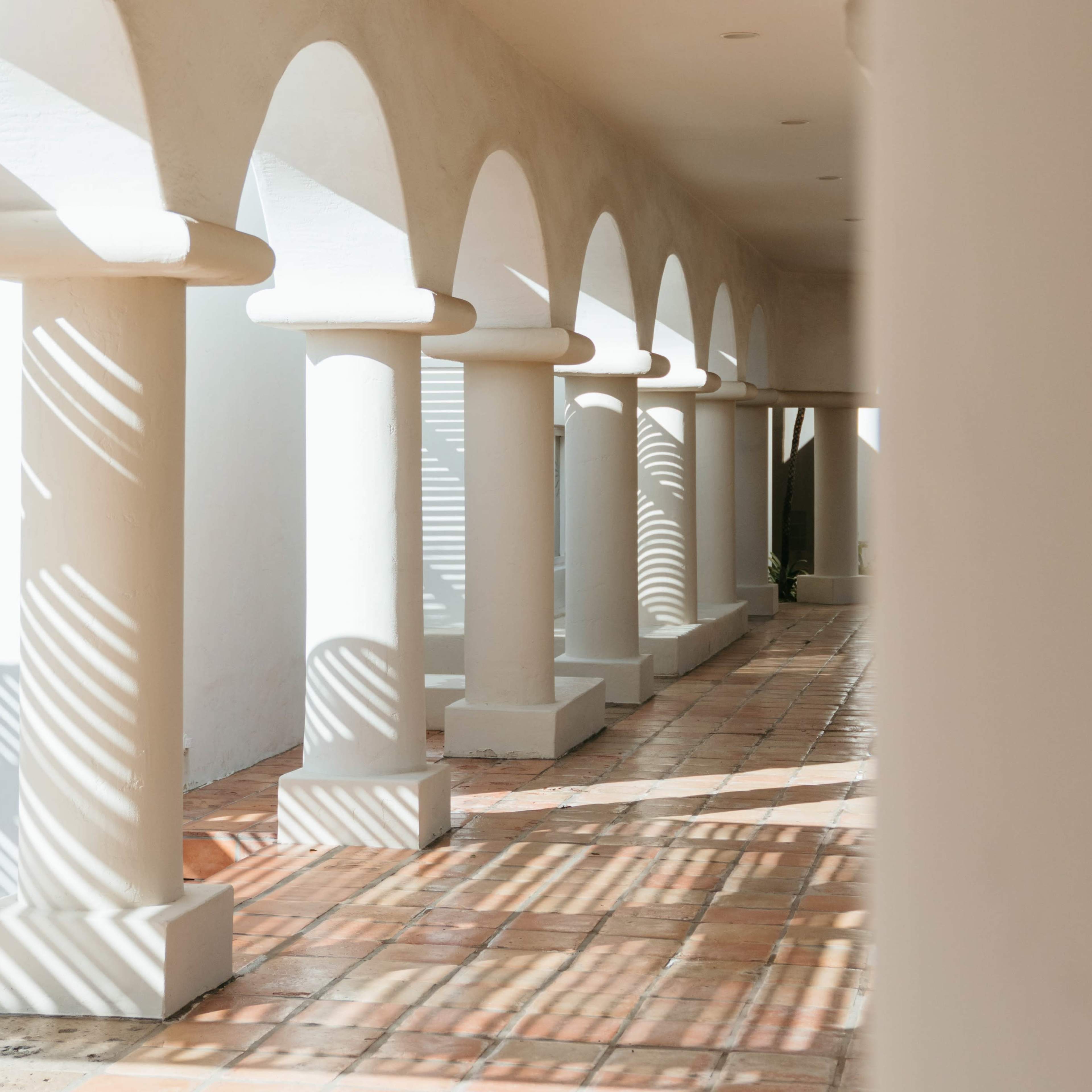 A corridor with arched columns casting shadows on a tiled floor.