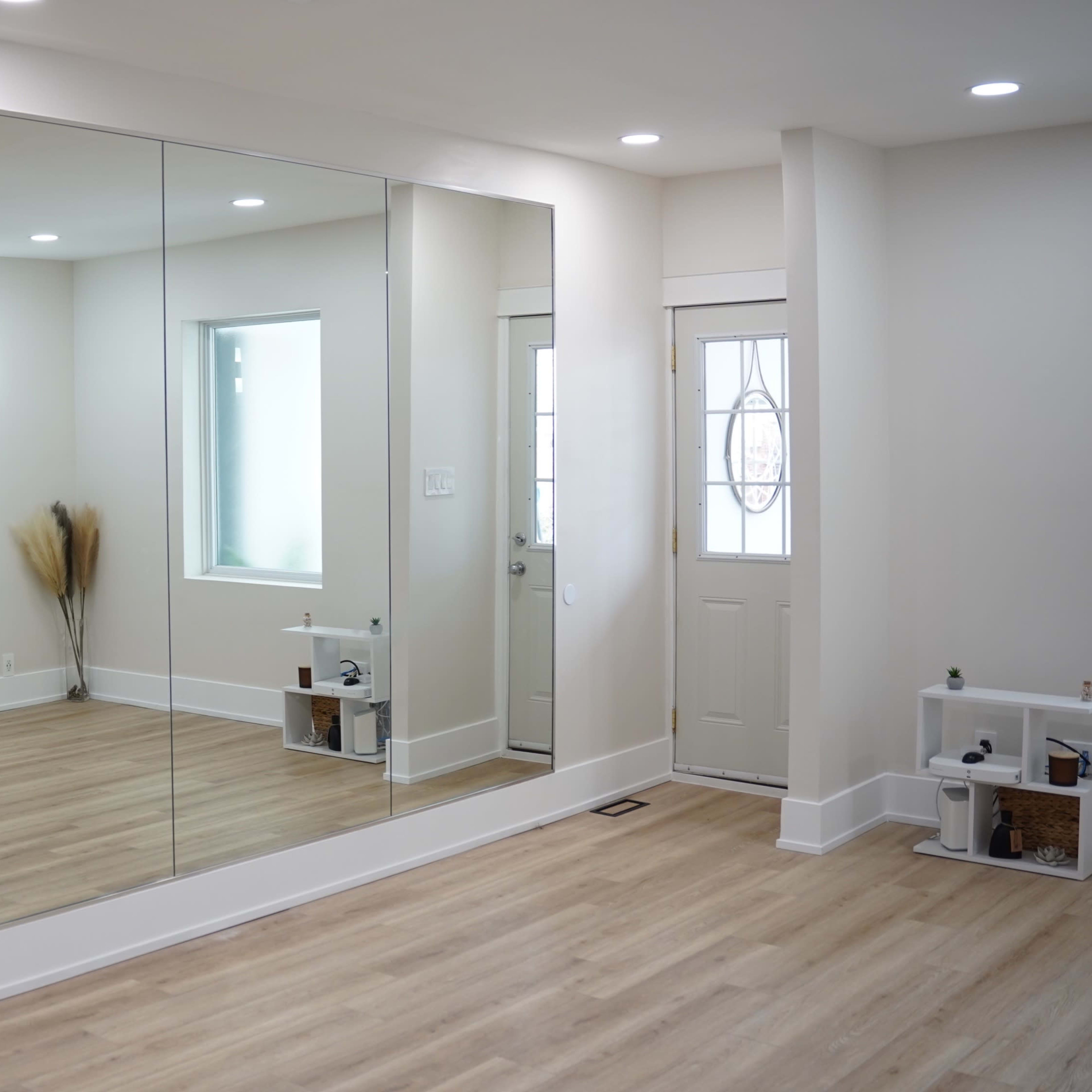 A spacious room features a large mirrored wall, a small television mounted on the opposite wall, and a front door with a window beside it.