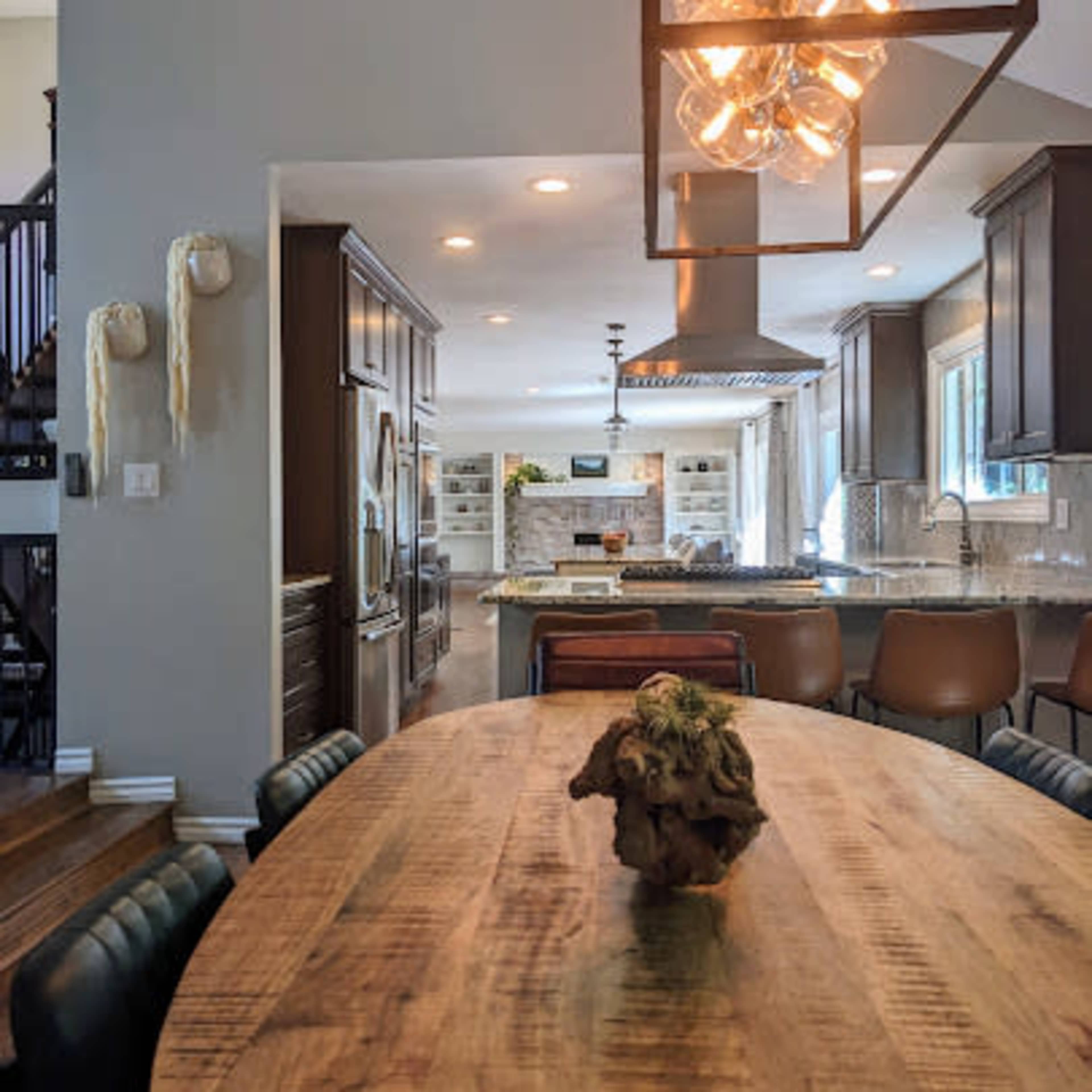 A spacious kitchen features a wooden dining table with a centerpiece, modern light fixtures, and sleek cabinetry.