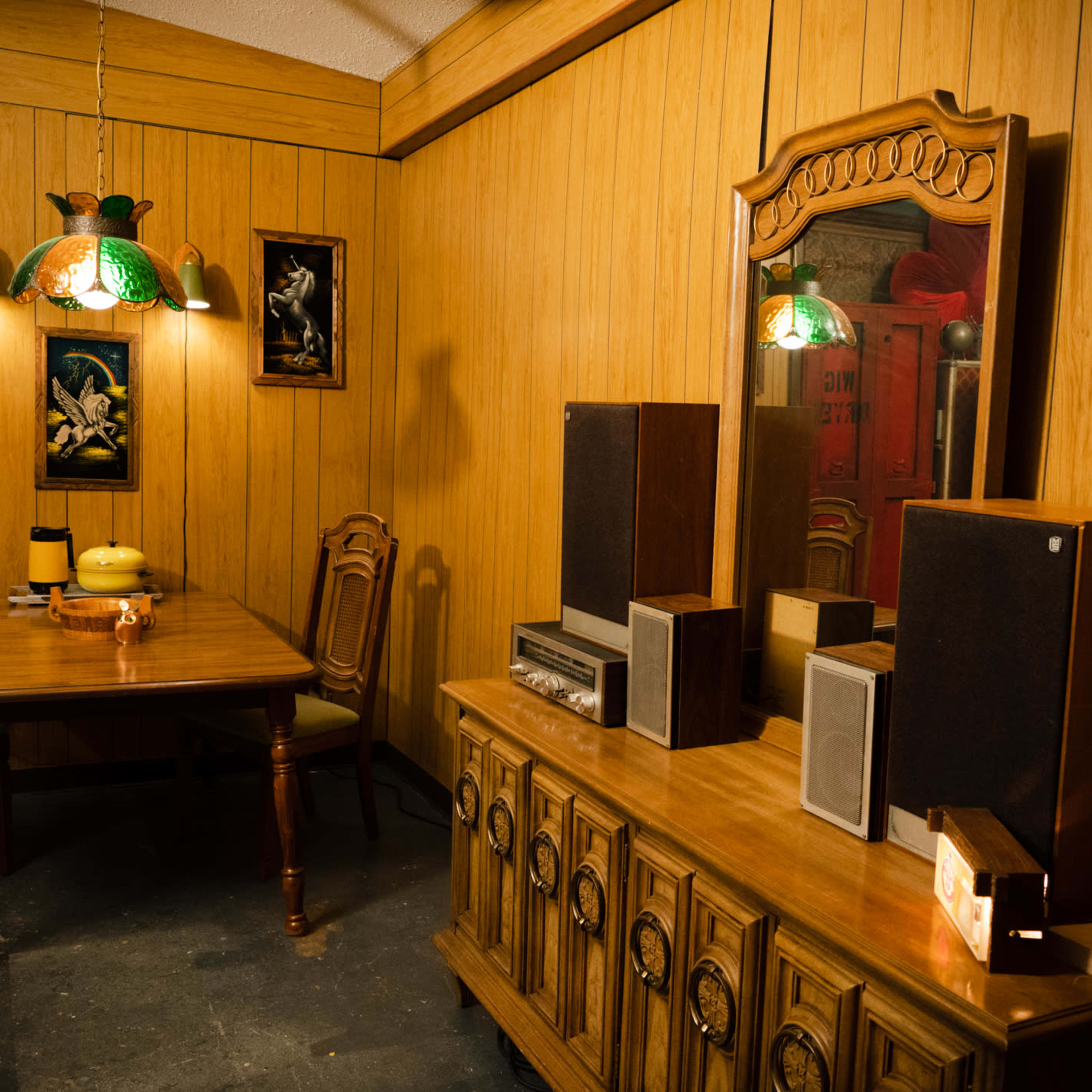A vintage-style dining area with a wooden table, chairs, and a sideboard, illuminated by an artistic hanging lamp.