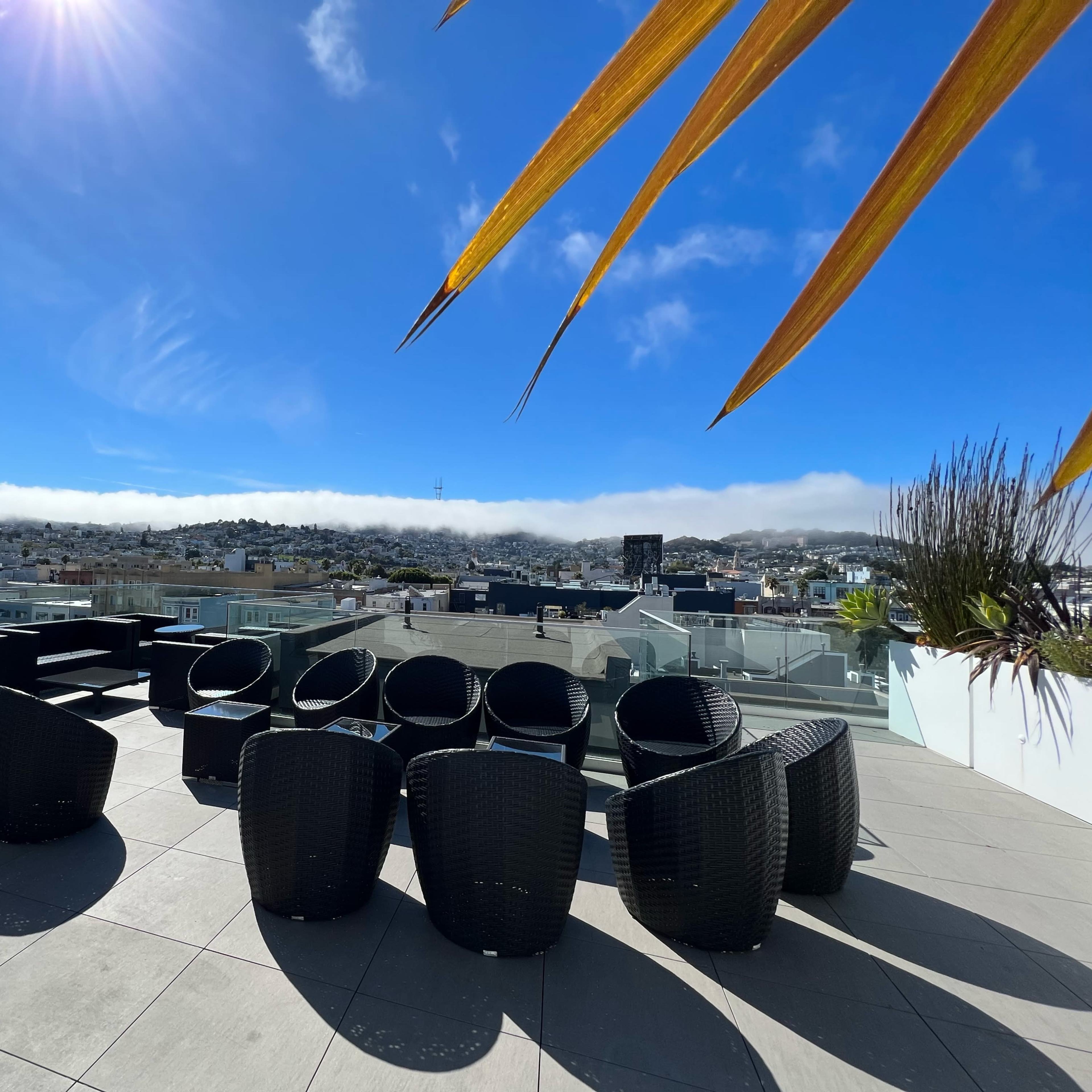A rooftop terrace with black wicker furniture set against a clear blue sky and distant rolling hills.