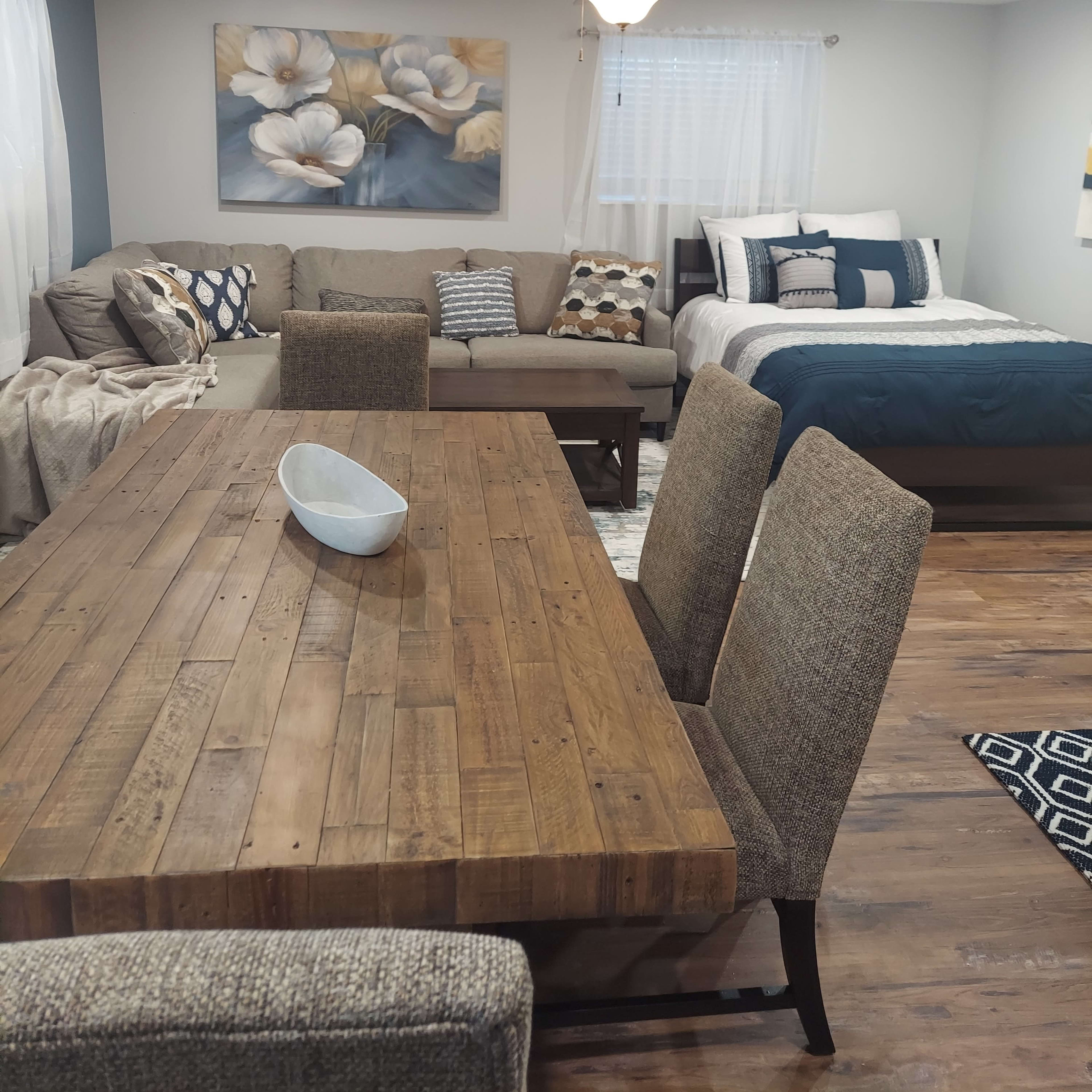 A cozy, combined living and sleeping area featuring a sectional sofa, a dining table, and a bed with blue and white bedding.