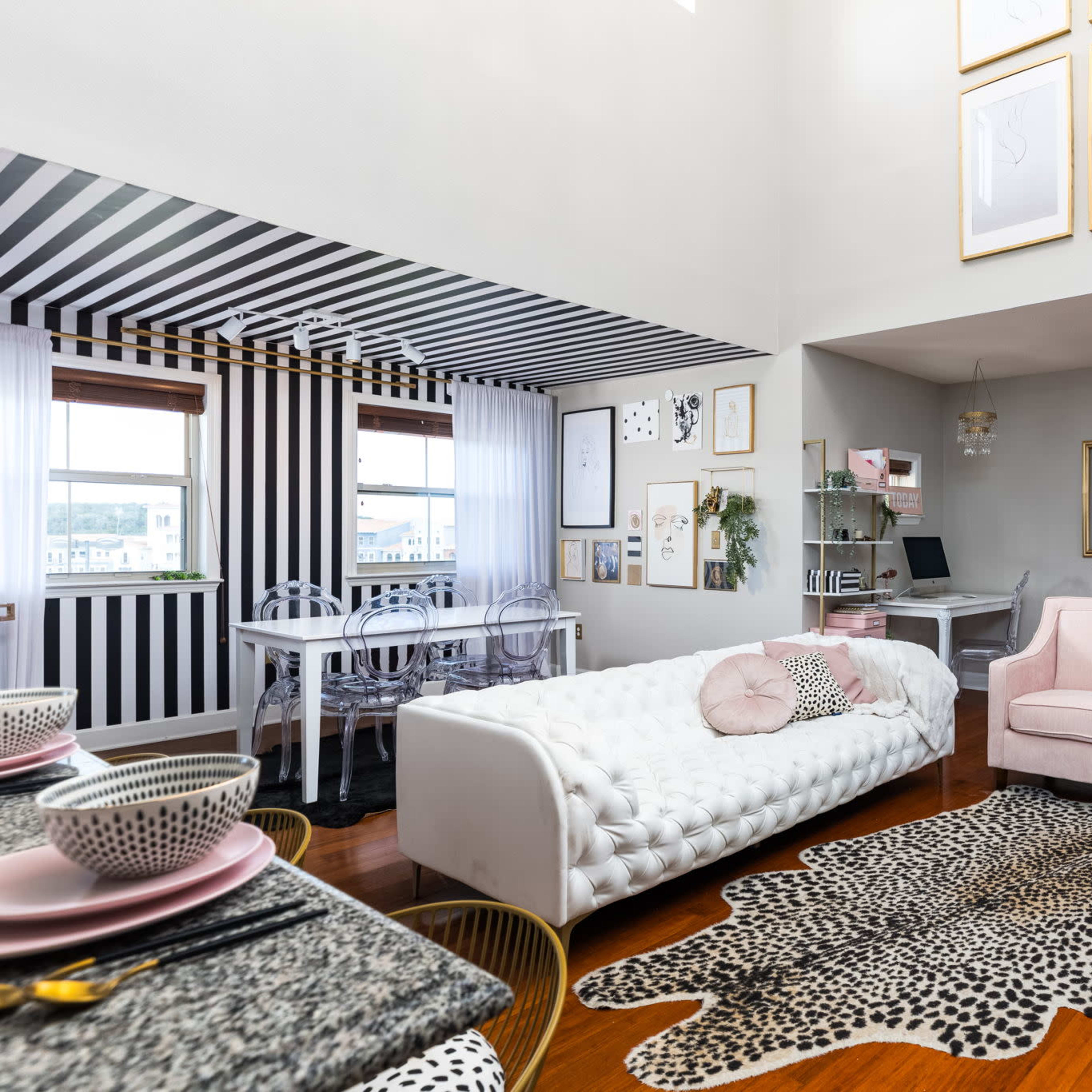 A modern living space with a striped accent wall, a white tufted sofa, a leopard print rug, and a dining area featuring a round table and chairs.