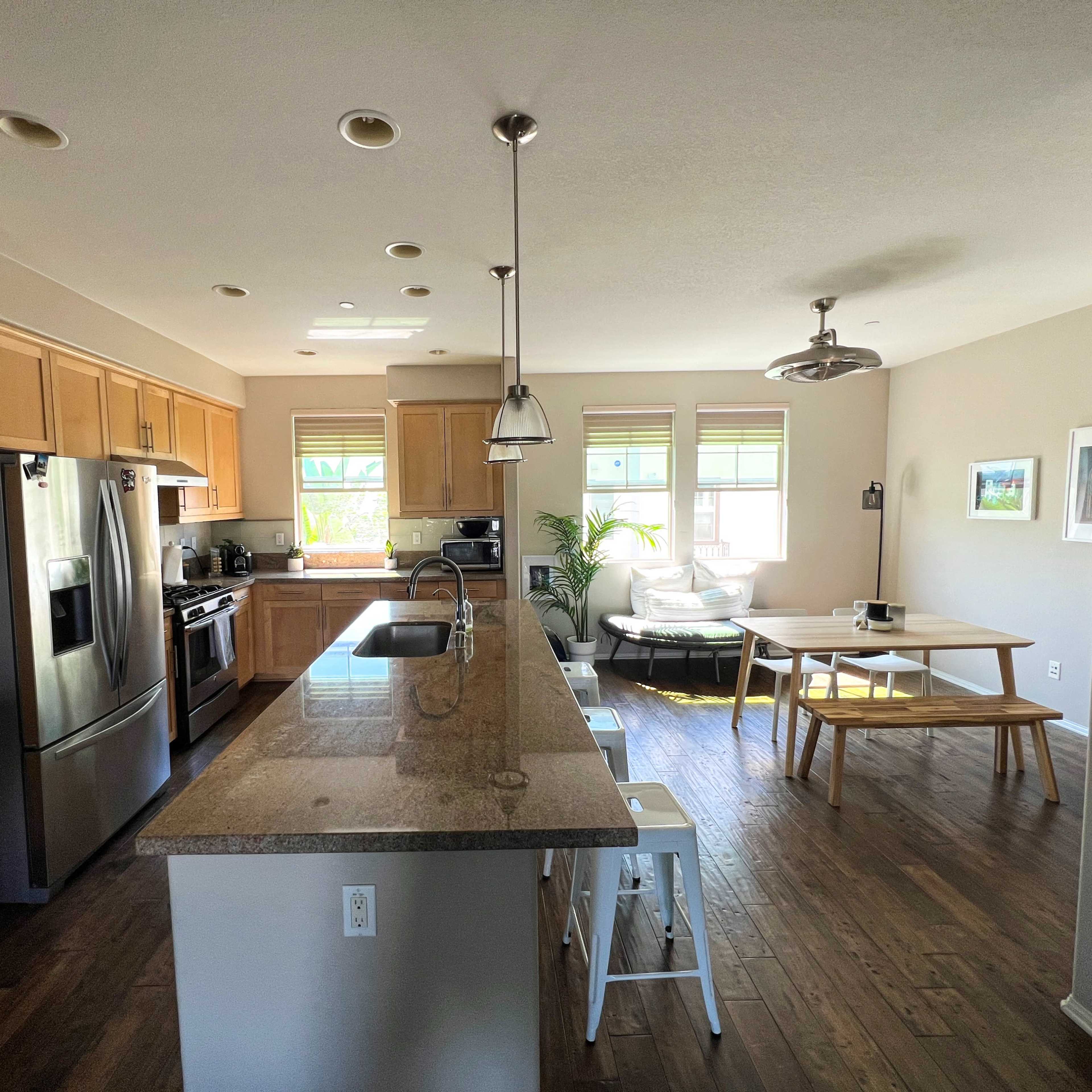 The kitchen features wooden cabinets, stainless steel appliances, a large island with seating, and connects to a dining area with a table and chairs.
