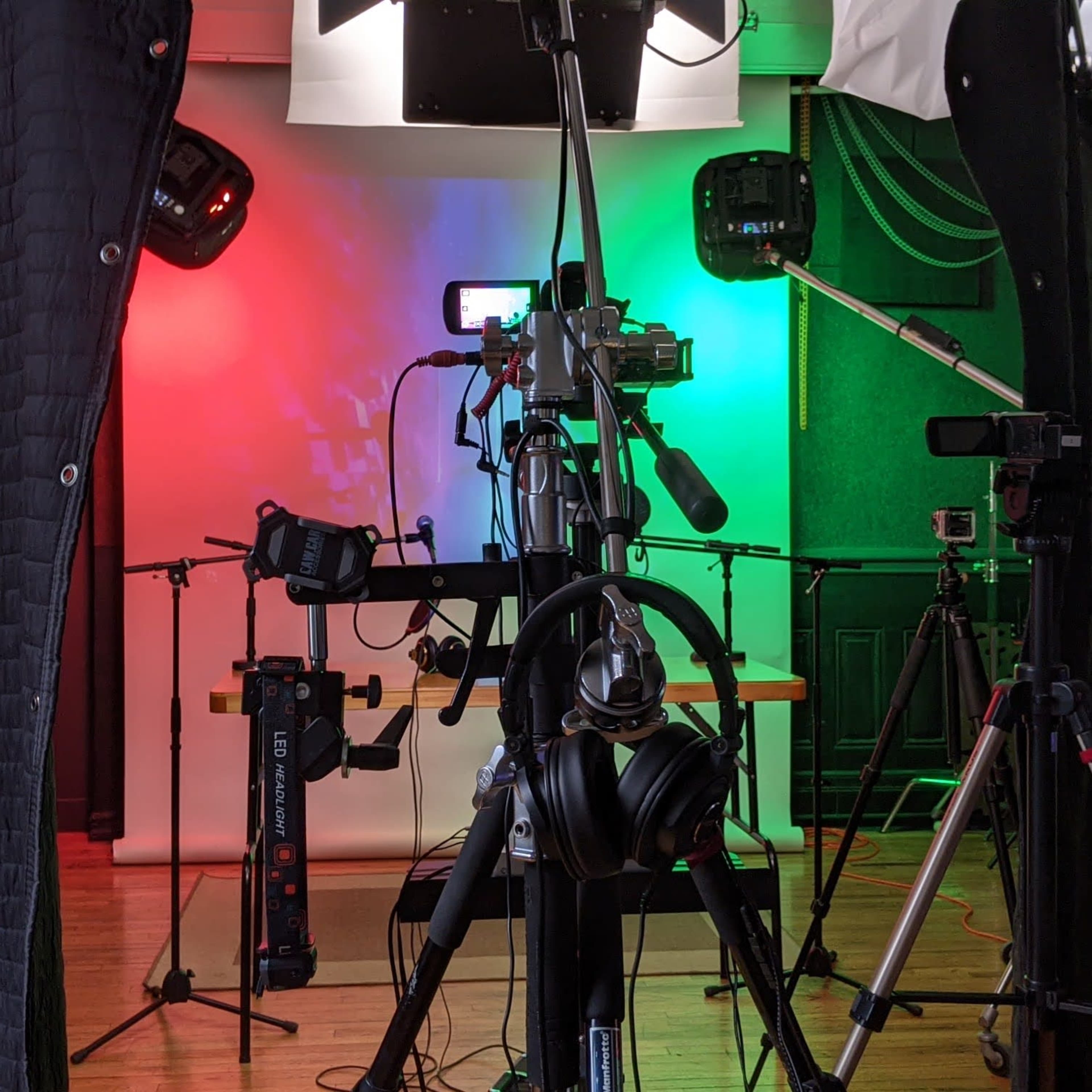 A photography or video recording setup with multiple cameras, lights, and audio equipment arranged on tripods in a studio space.