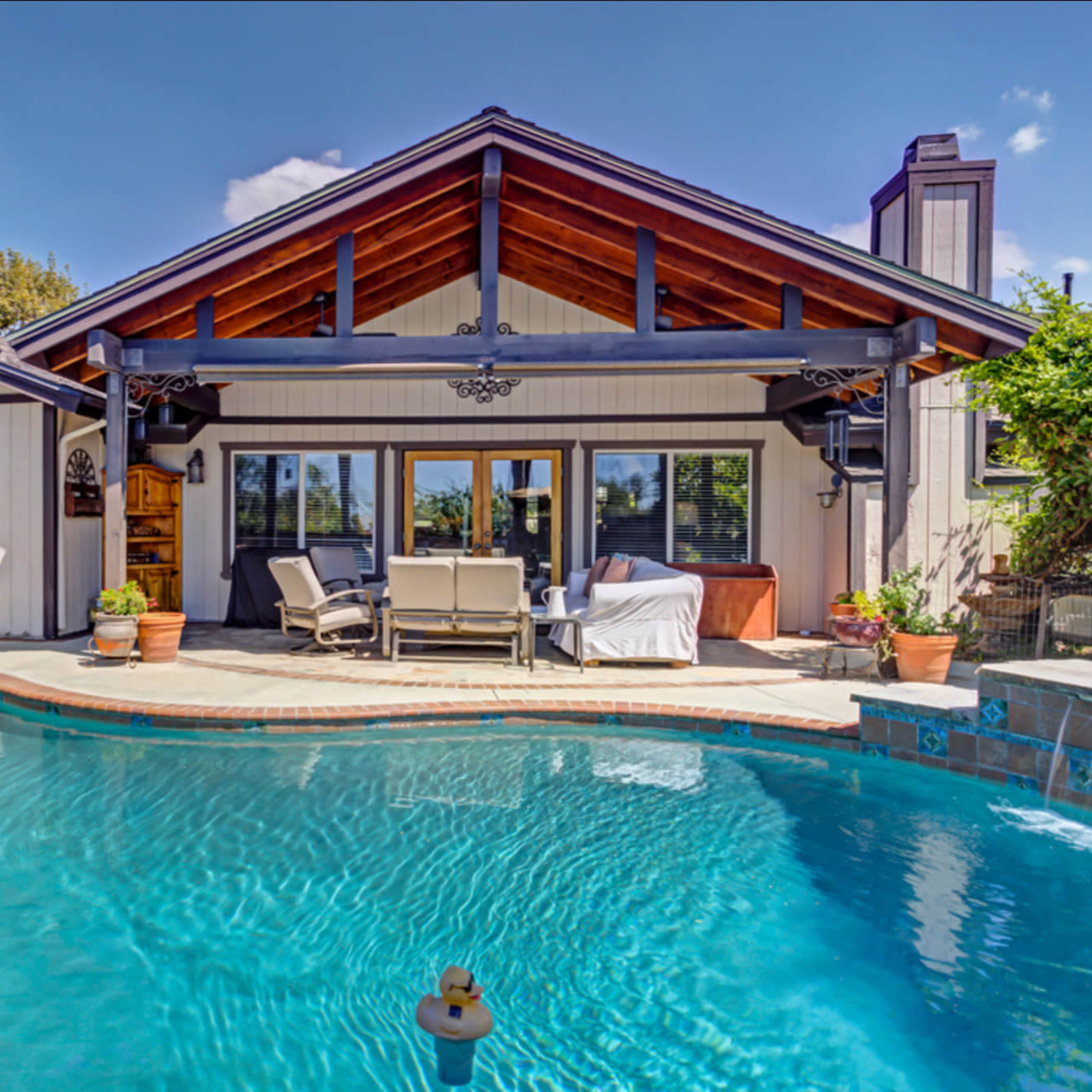 A modern home with a landscaped backyard features a swimming pool and outdoor seating area under a covered patio.