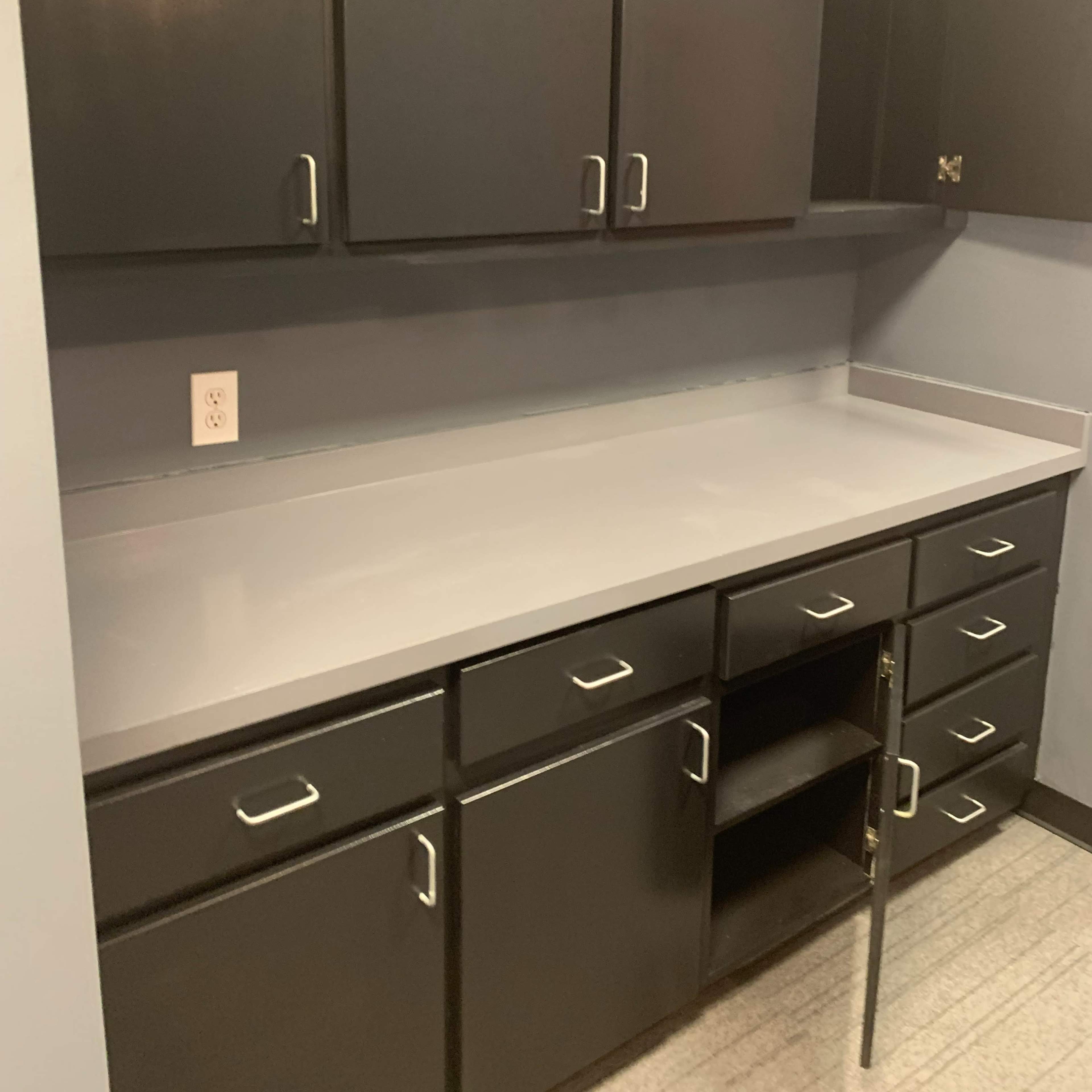 A kitchen space with dark cabinets above and below a gray countertop, featuring a central cabinet with an open space.