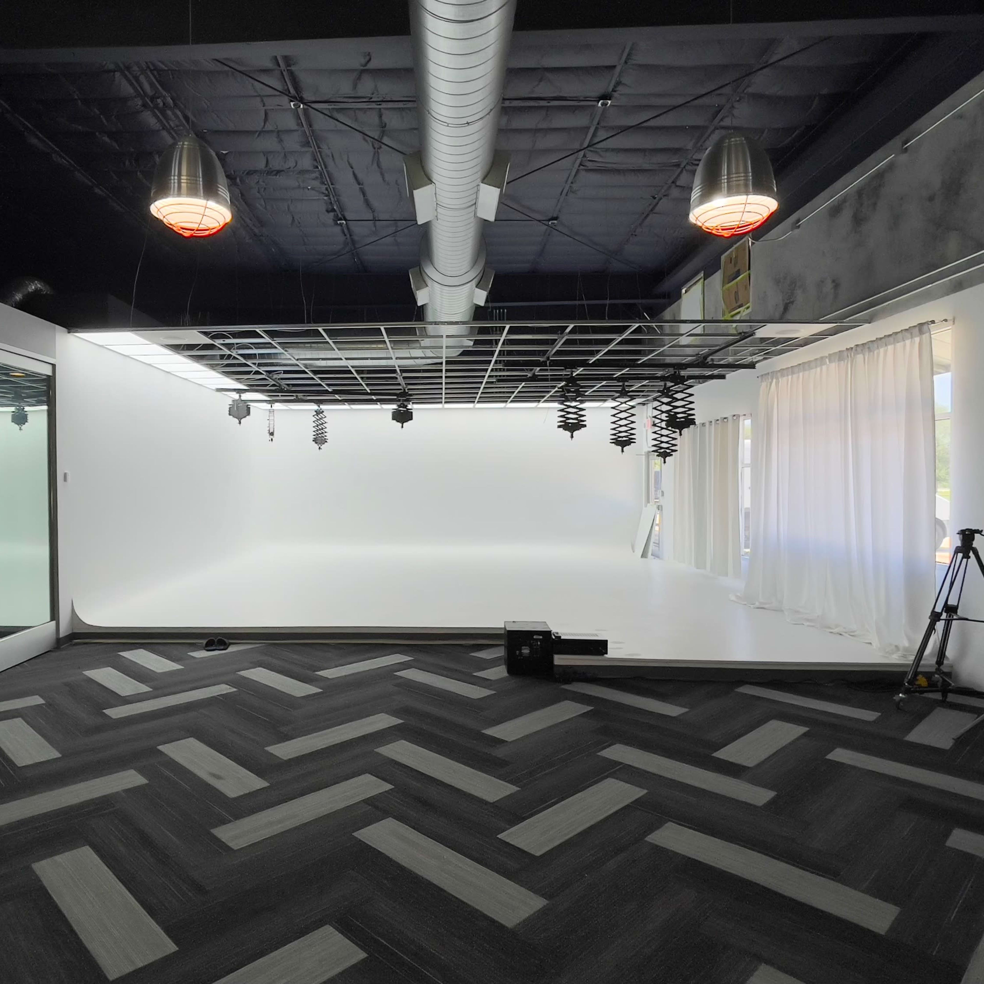 A spacious studio with a white backdrop, large windows, and a herringbone-patterned floor.