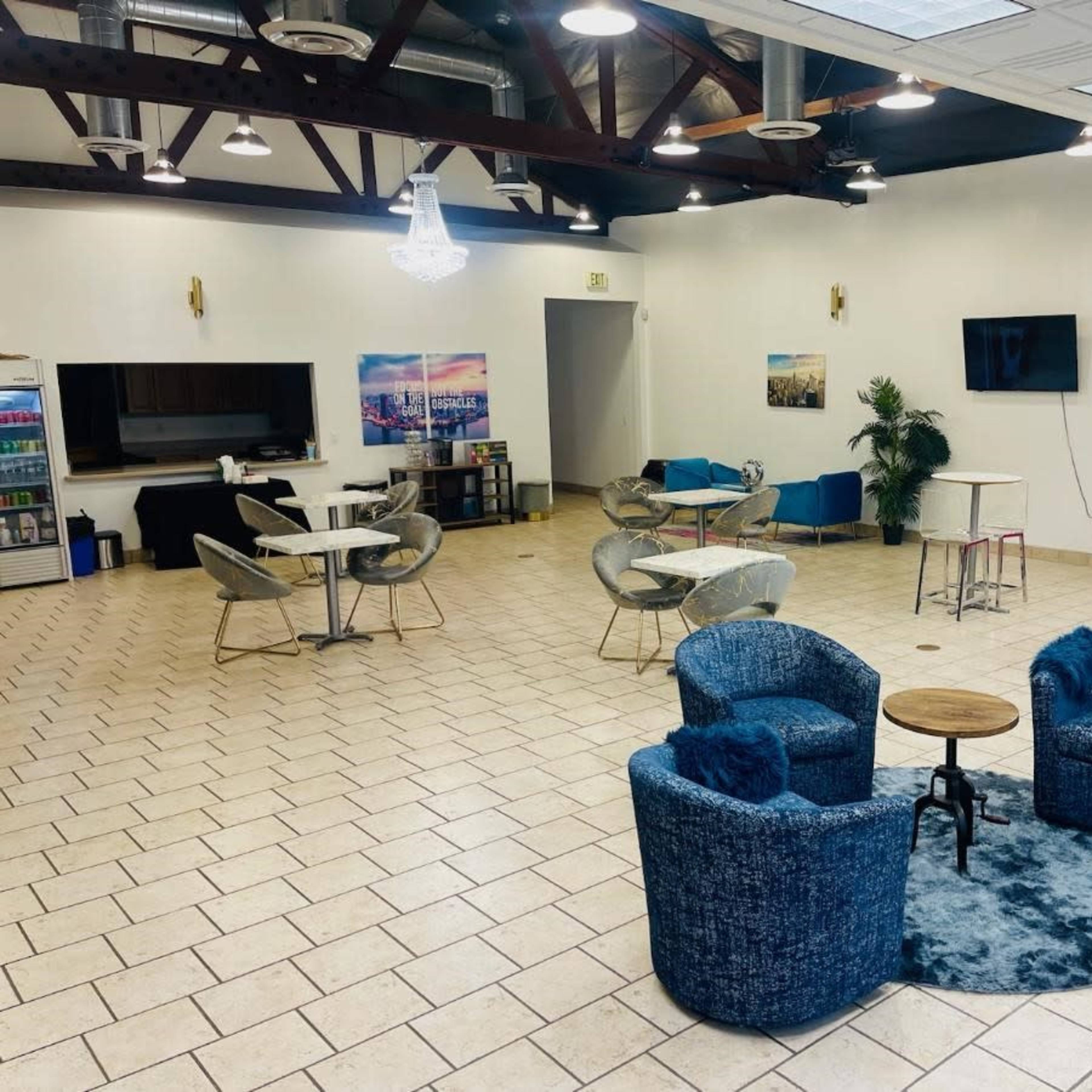 A spacious indoor area with seating, including two blue upholstered chairs and a small round table, surrounded by other furniture and decor.
