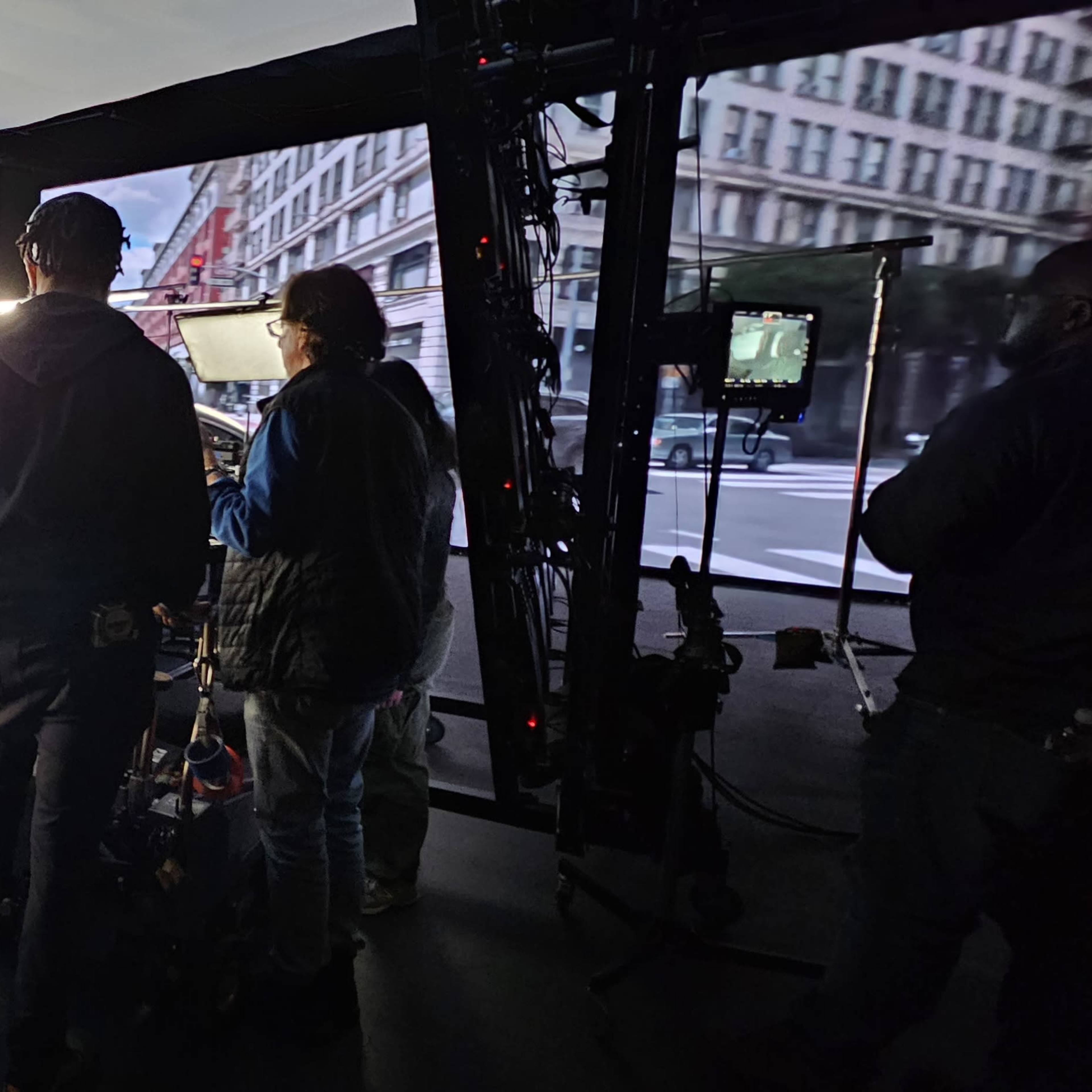 A film crew is set up inside a studio, preparing to shoot a scene featuring a car under controlled lighting conditions.