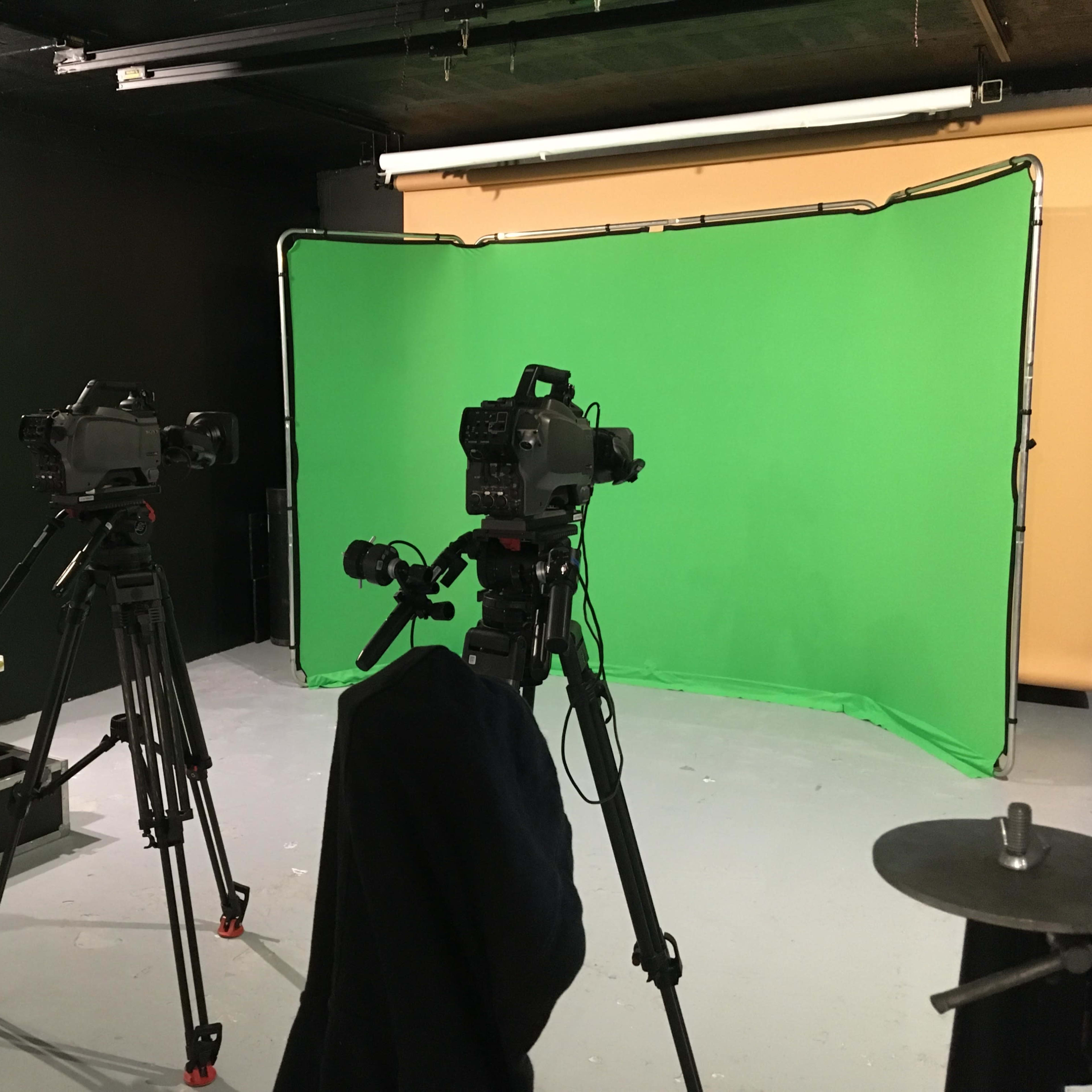 A video production setup with two cameras on tripods facing a green screen in a studio environment.