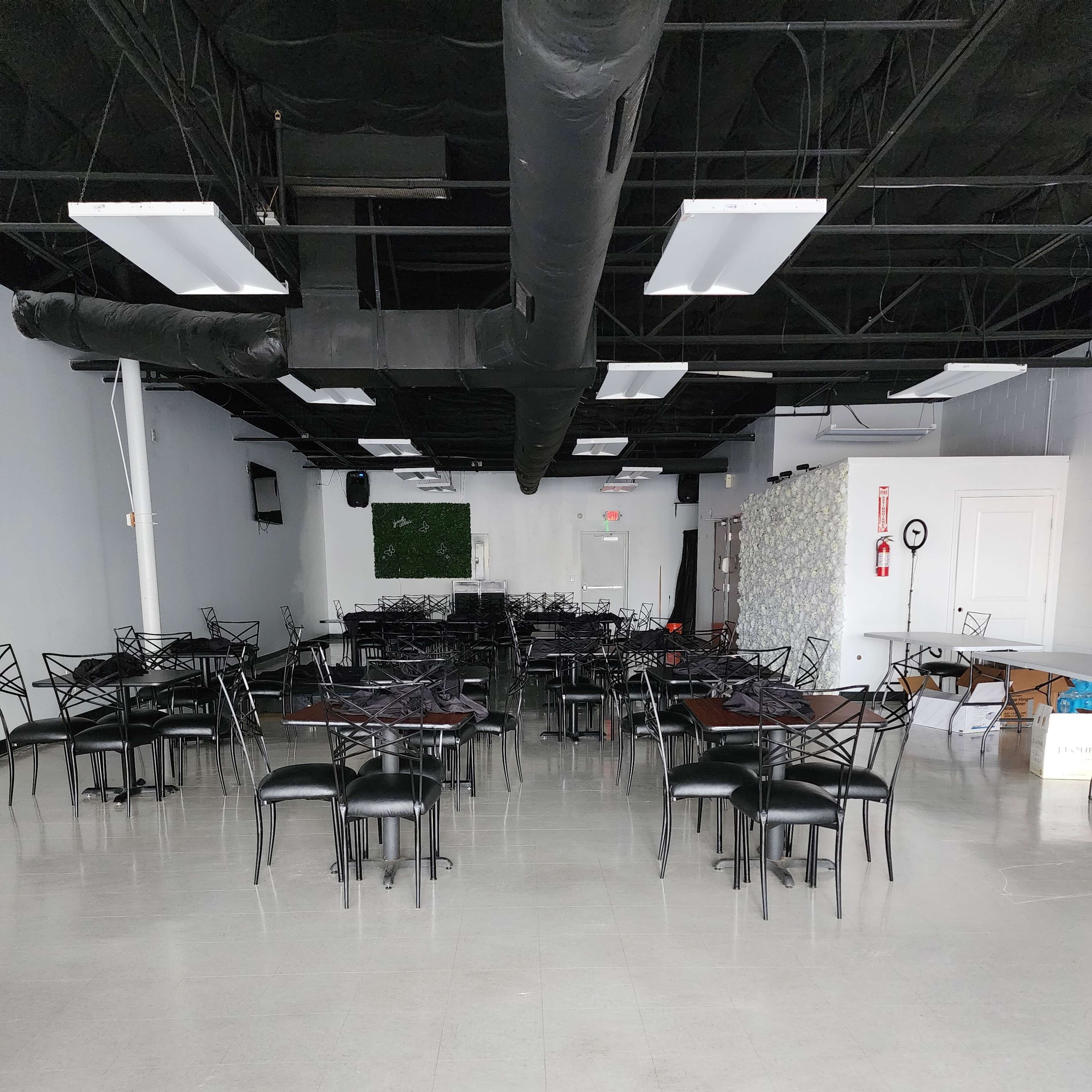 An empty dining area with several black chairs and tables arranged in rows on a light-colored floor.
