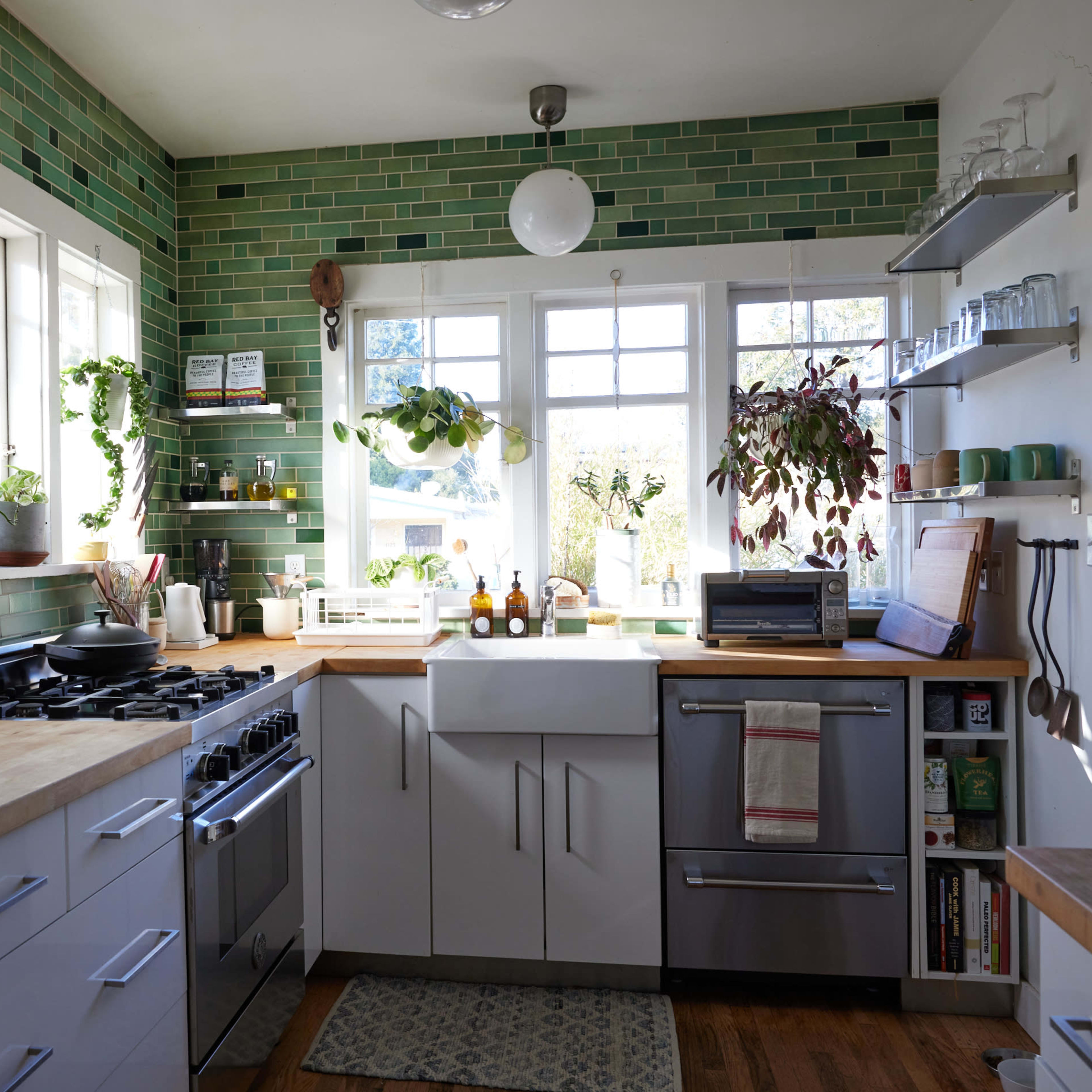 A modern kitchen with green tiled walls, a large window, and stainless steel appliances.