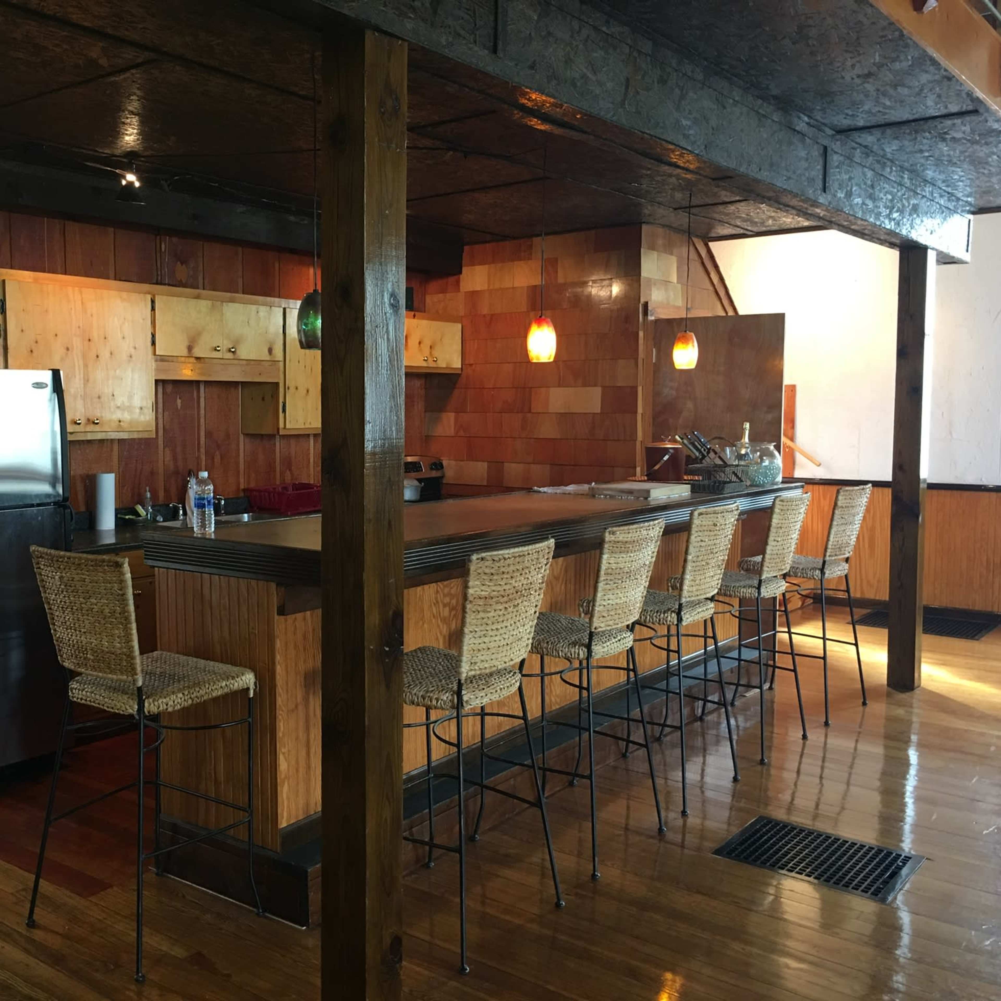 A modern kitchen with a long bar area featuring high stools, wooden cabinets, and a stainless steel refrigerator.