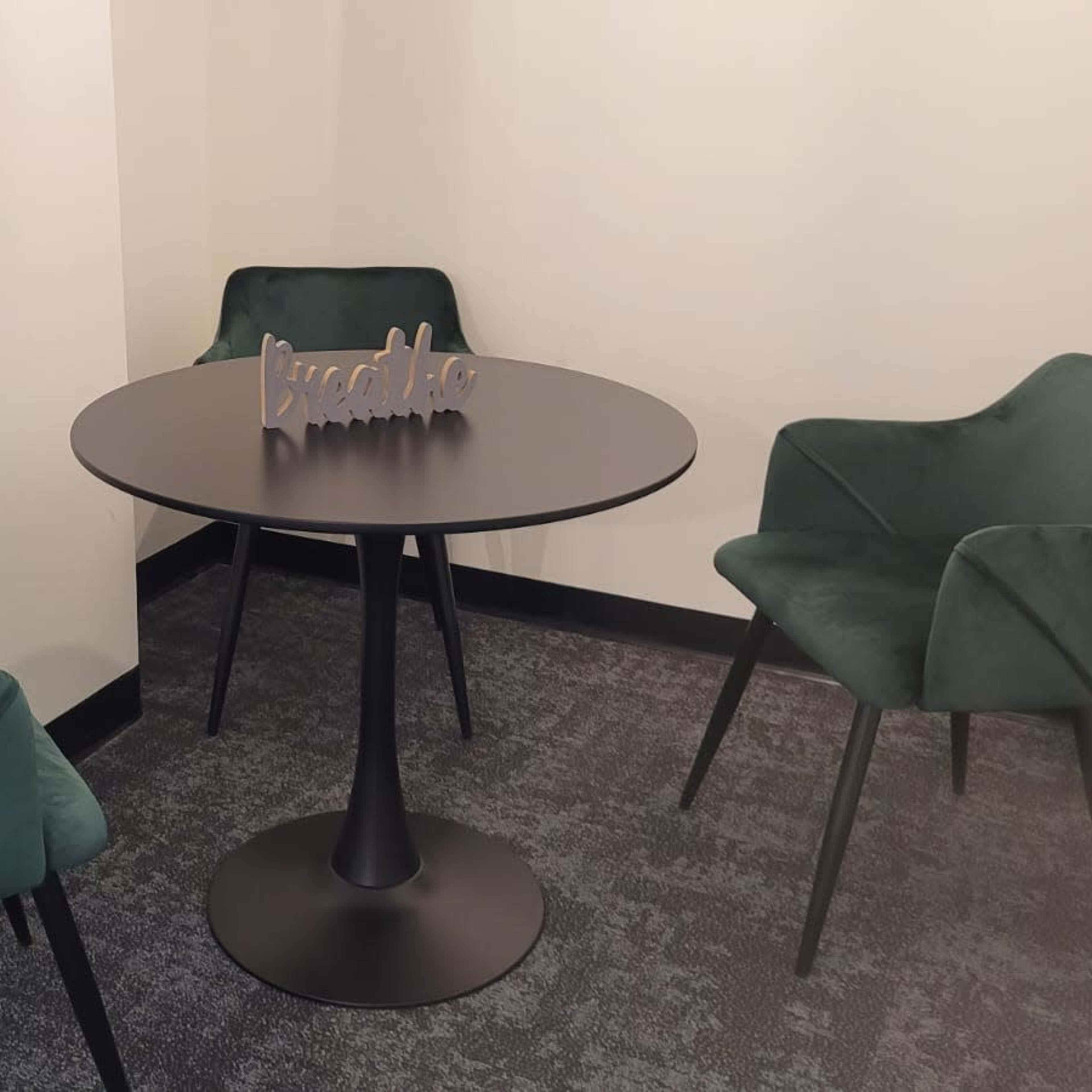 A small meeting area features a round black table surrounded by three green velvet chairs.