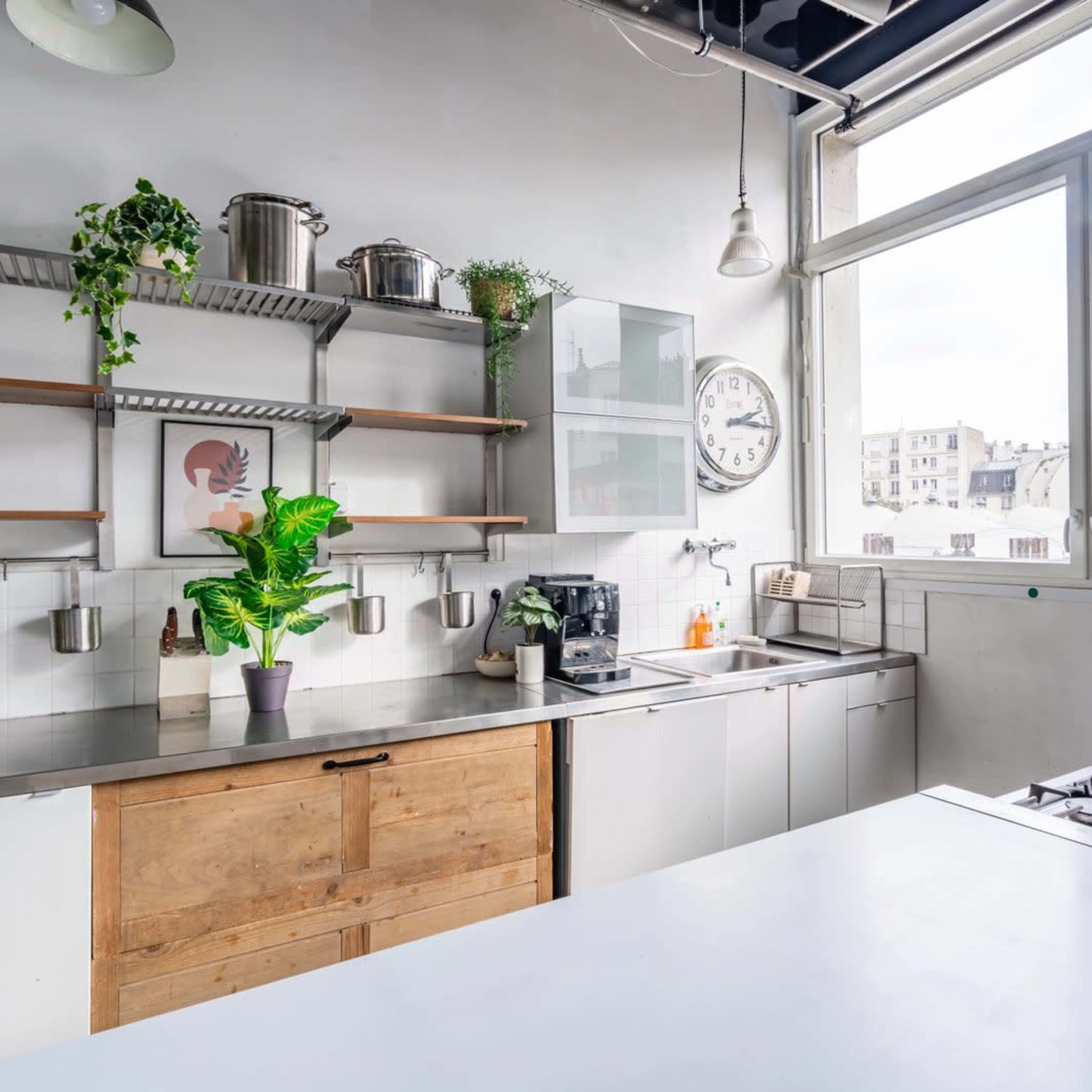 A modern kitchen features stainless steel countertops, wooden cabinetry, and large windows that provide natural light.