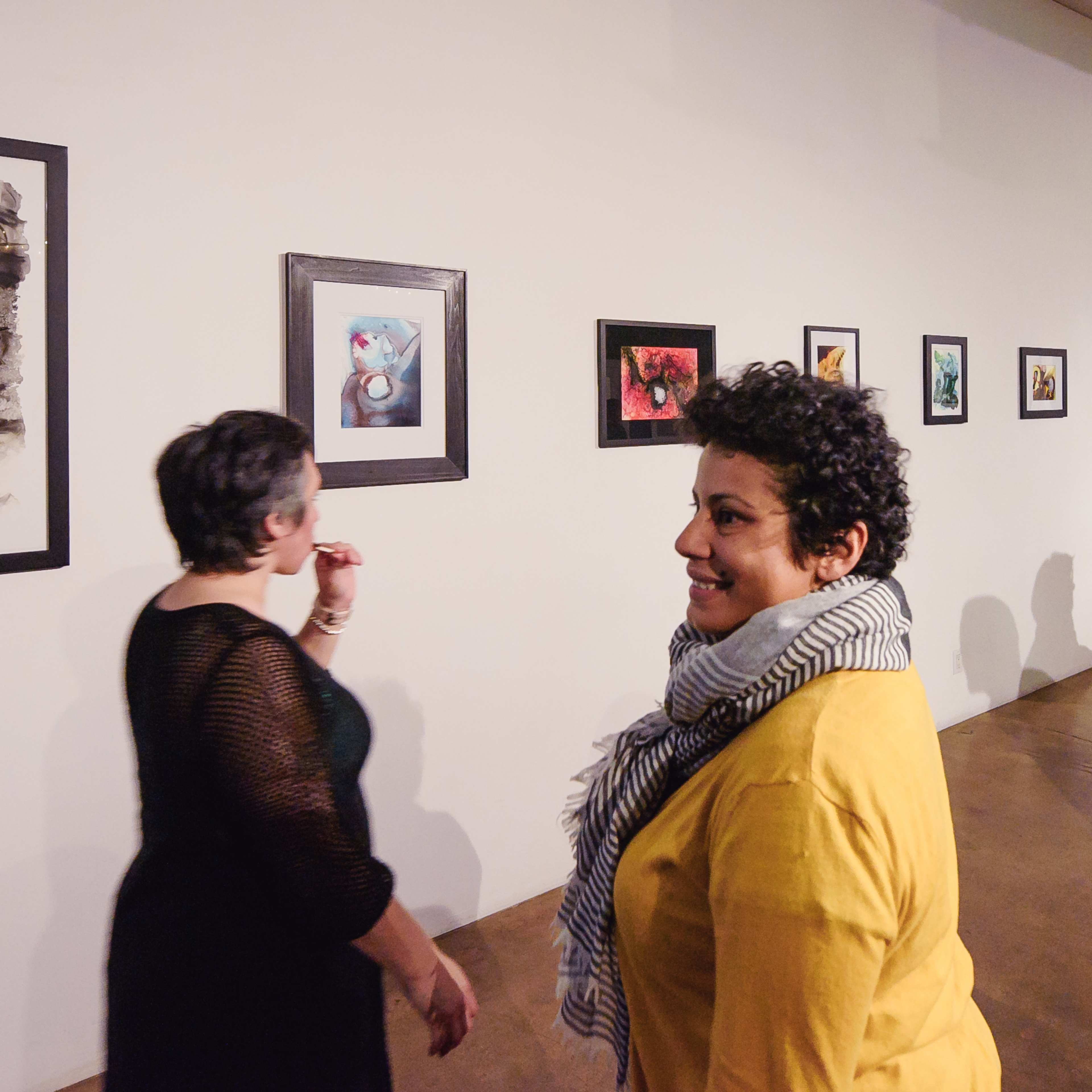 People are exploring an art gallery with various framed artworks displayed on the wall.