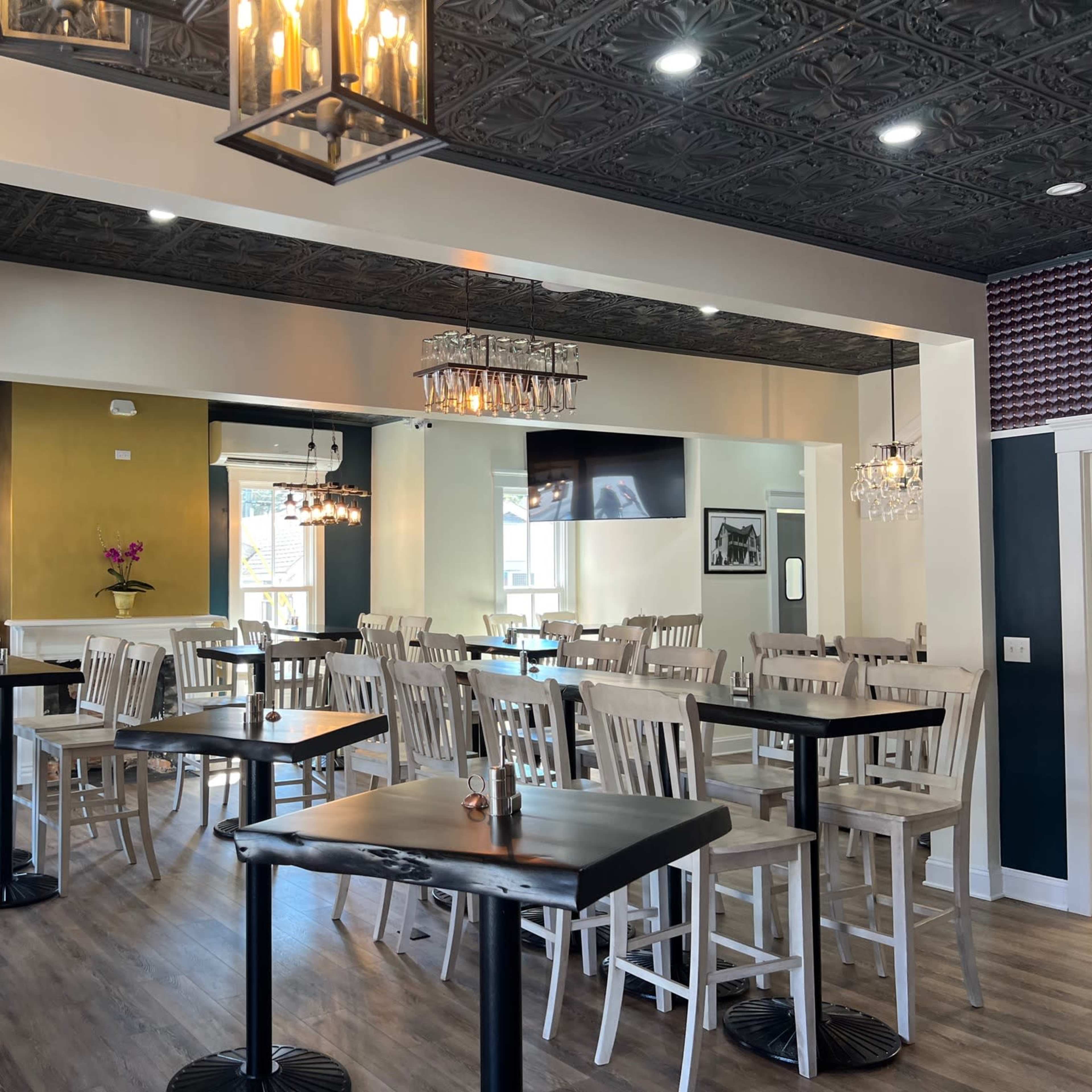 A restaurant interior with wooden tables and chairs, pendant lighting, and a mirrored wall reflecting the seating area.