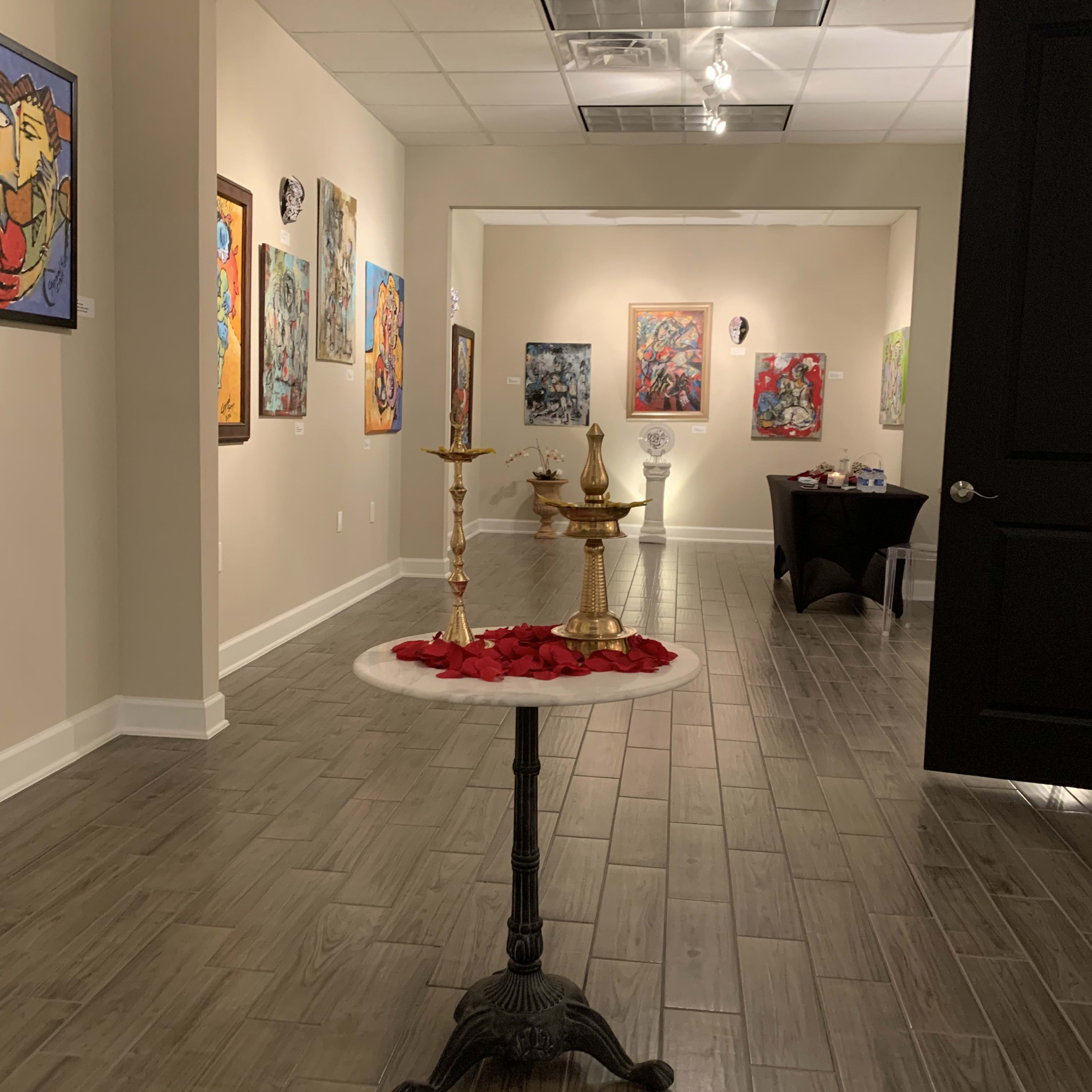 An art gallery with paintings displayed on the walls and a table in the foreground adorned with candles and rose petals.