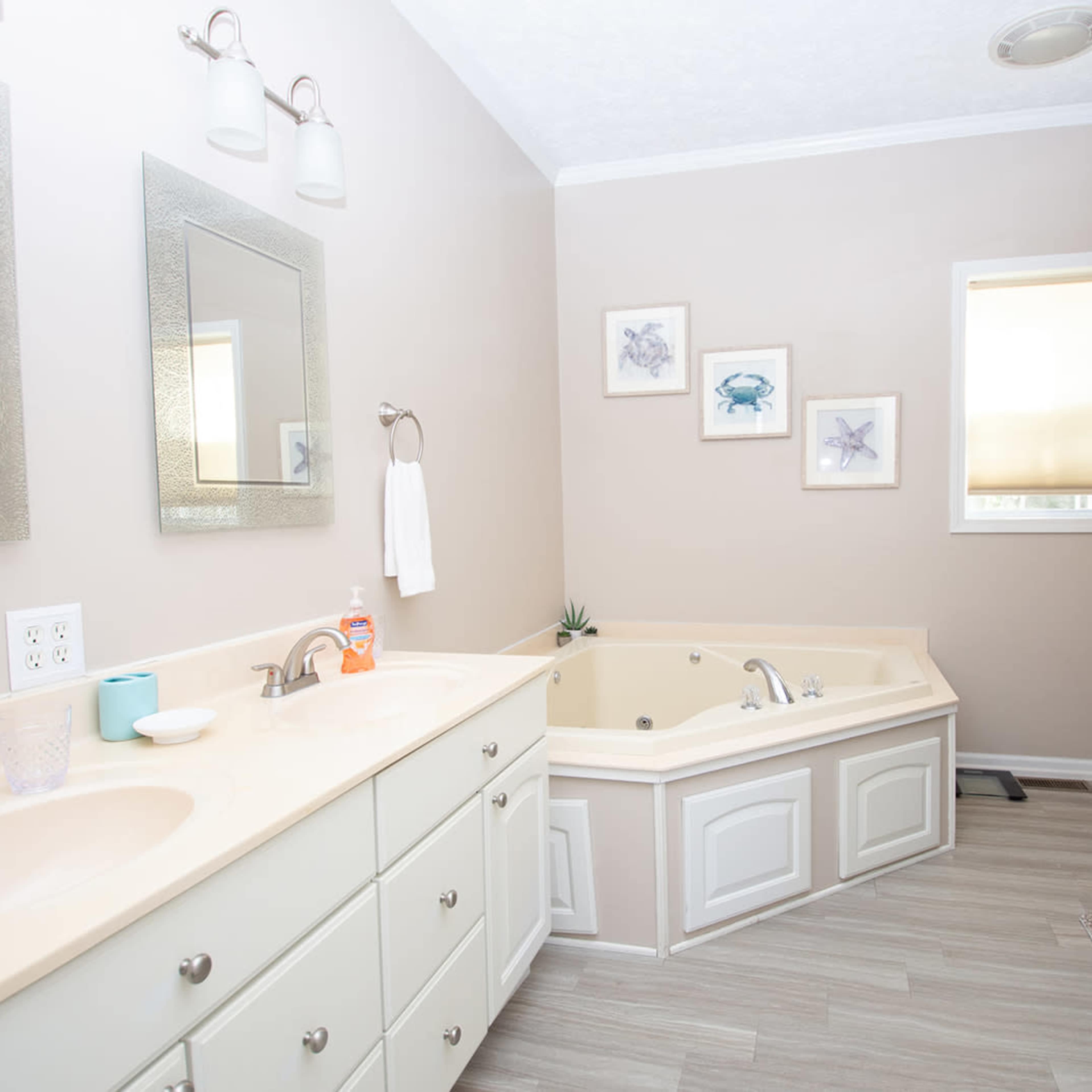 A bathroom features dual sinks, a large corner bathtub, and framed artwork depicting marine life.