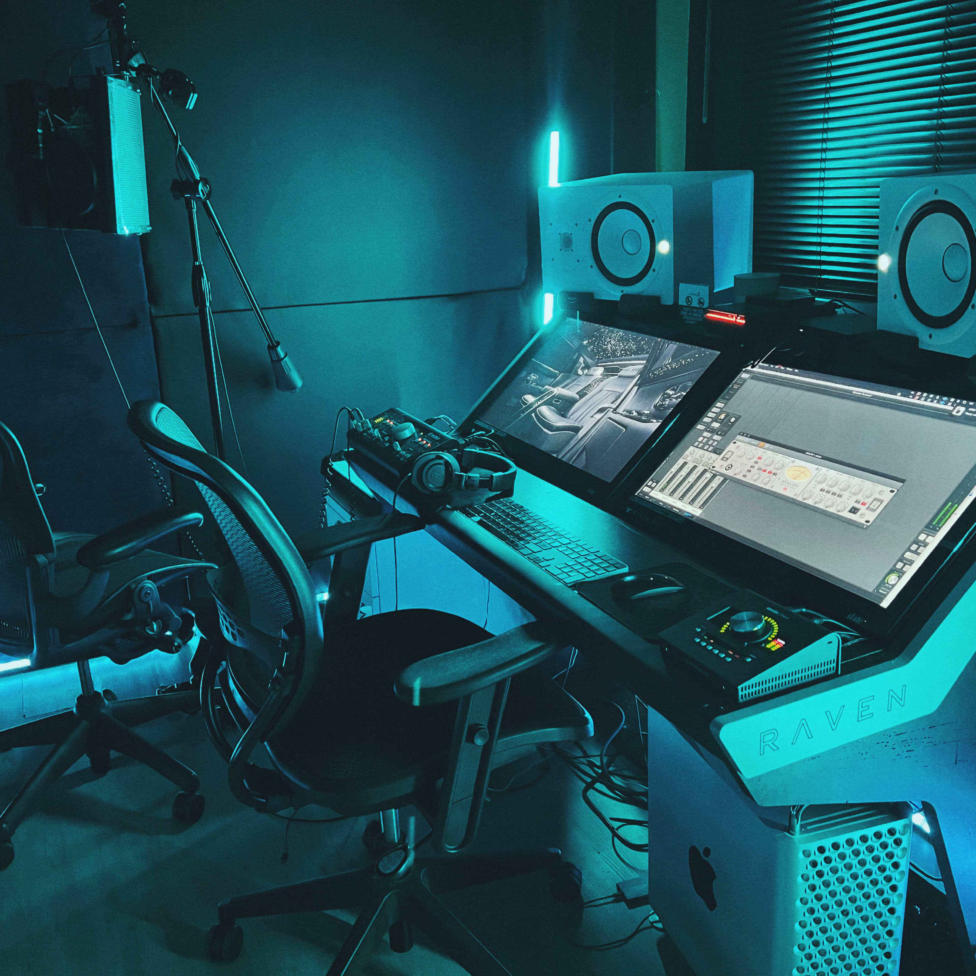 A music production studio with a sleek desk setup featuring dual monitors, speakers, and various audio equipment under soft blue lighting.