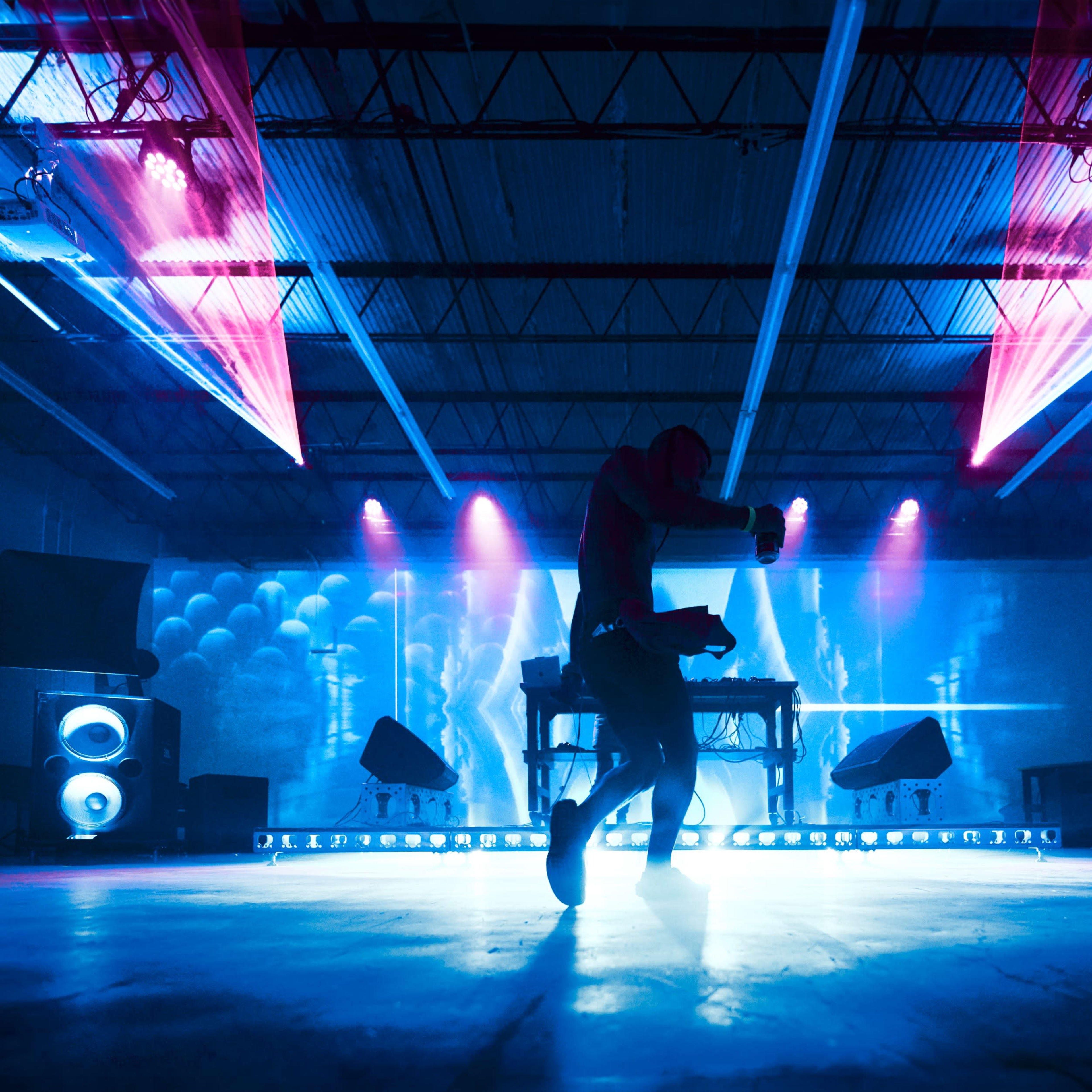 A dancer performs on a stage illuminated by colorful lights in an industrial space.