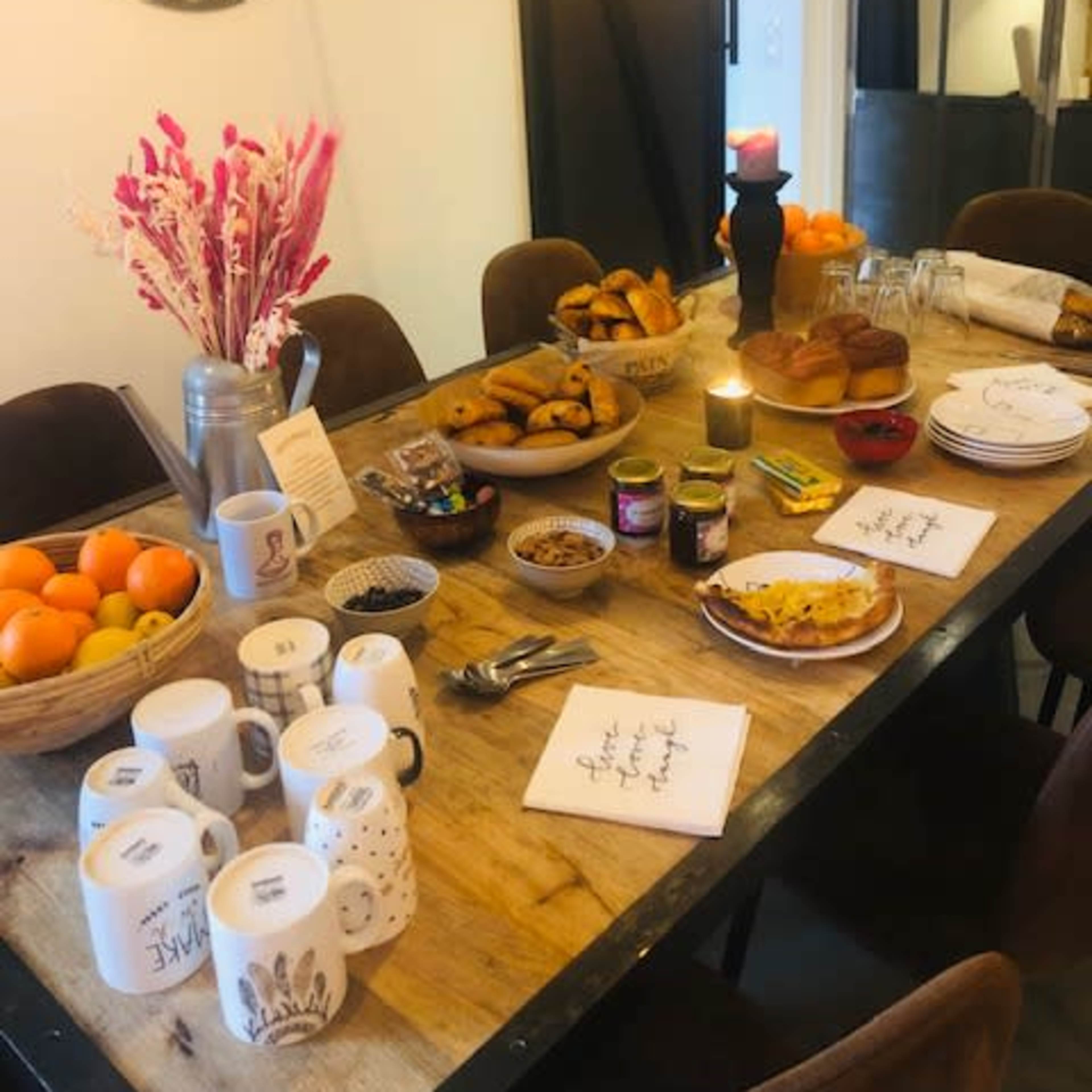 A dining table is set with a variety of breakfast items, including pastries, fruit, and drinks, alongside decorative tableware and candles.