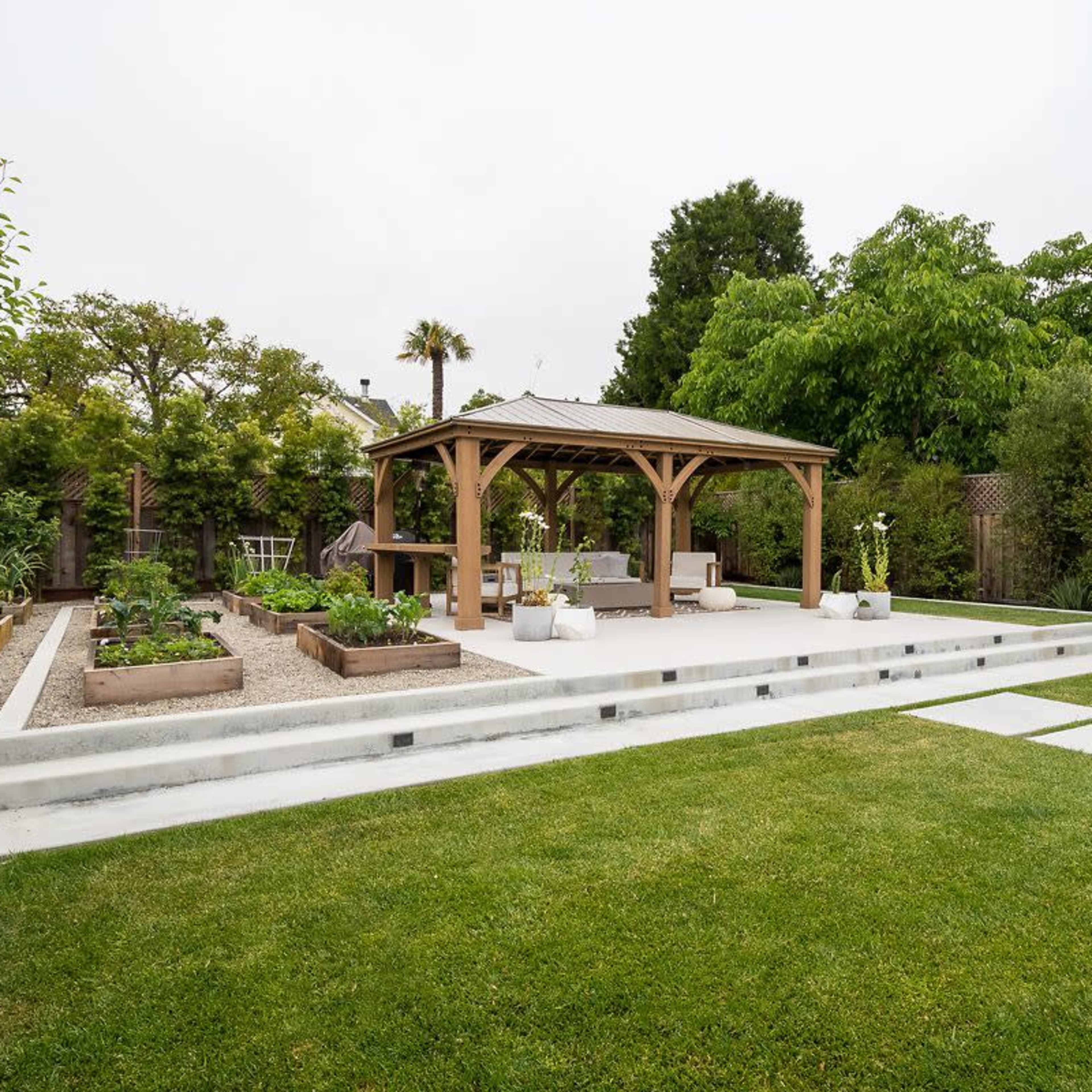 A landscaped backyard featuring a wooden gazebo, garden beds, and a manicured lawn.