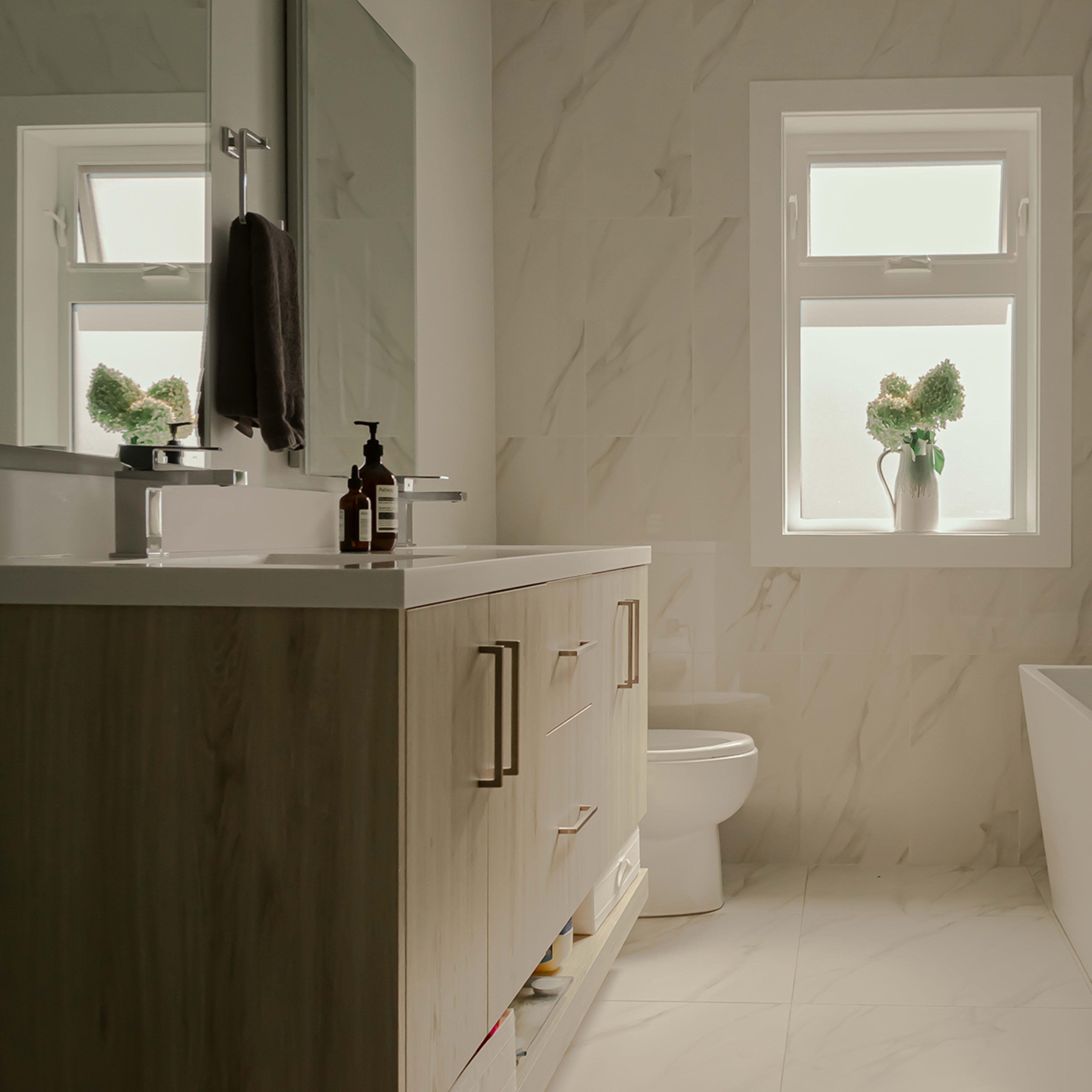 A modern bathroom featuring a bathtub, a sink with a cabinet, a toilet, and a window with a potted plant.