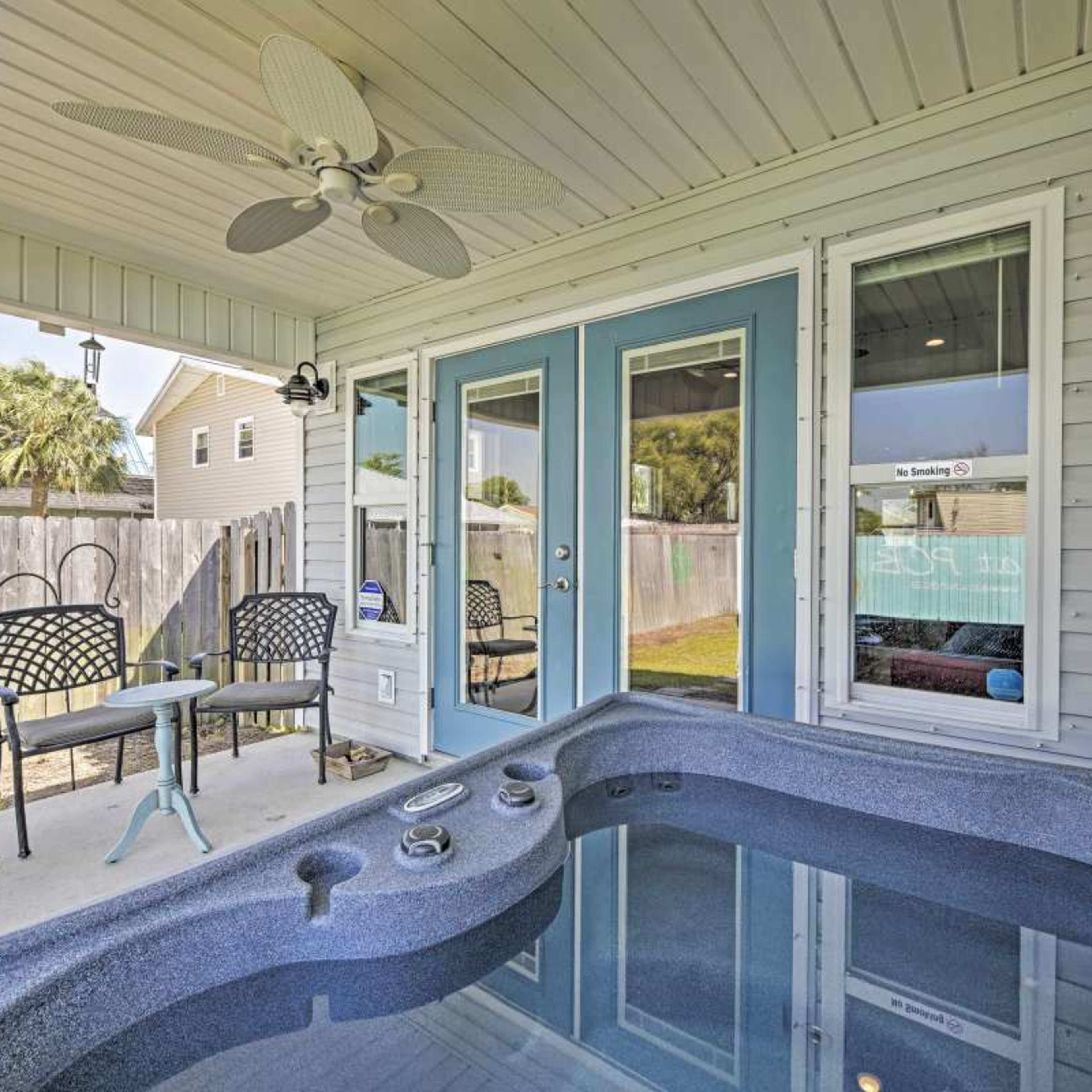 A hot tub beside a patio area with chairs, under a covered porch of a house.