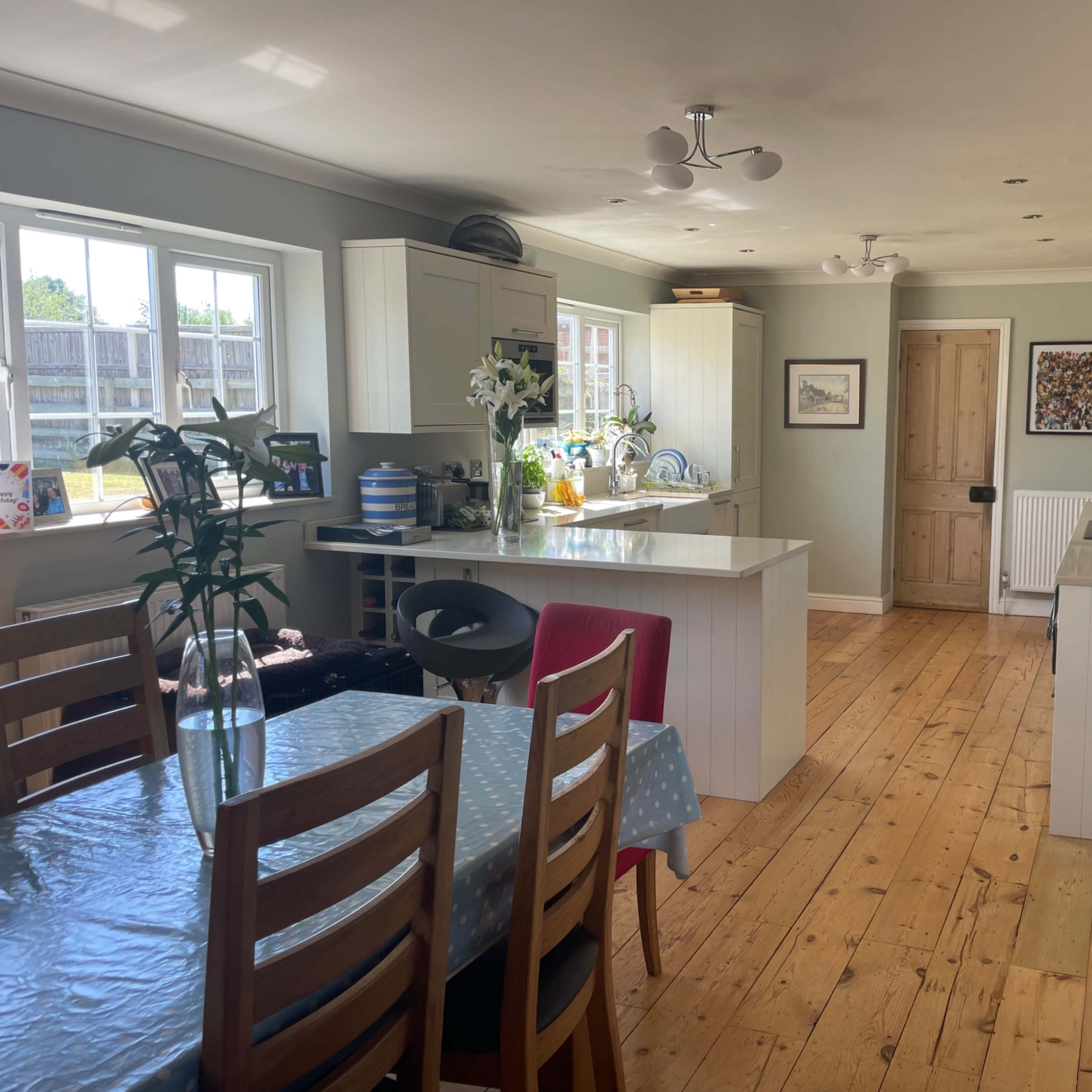 A brightly lit kitchen and dining area featuring wooden flooring, a table set for meals, and modern cabinetry.