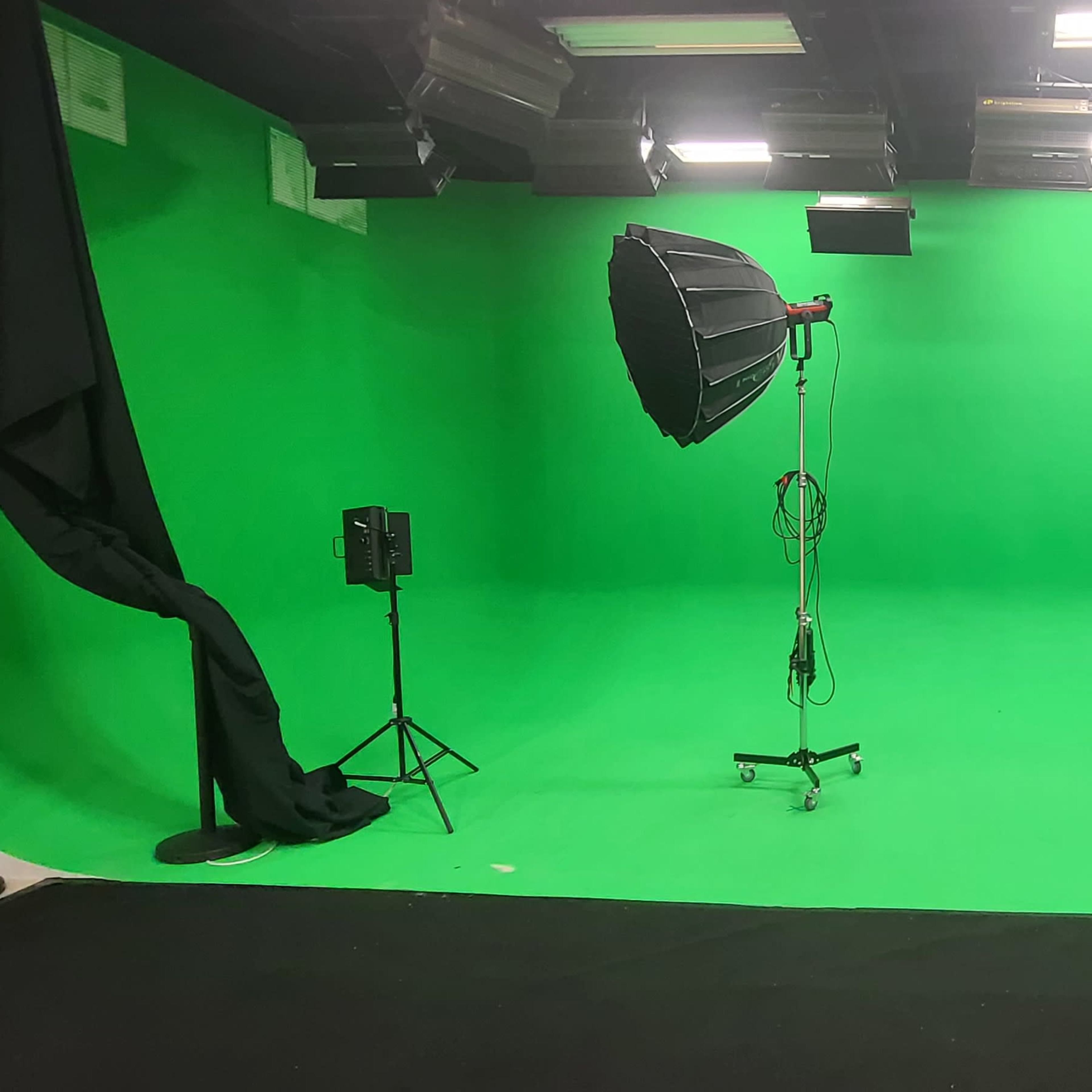 A green screen studio equipped with one large softbox light and two smaller lights on stands.