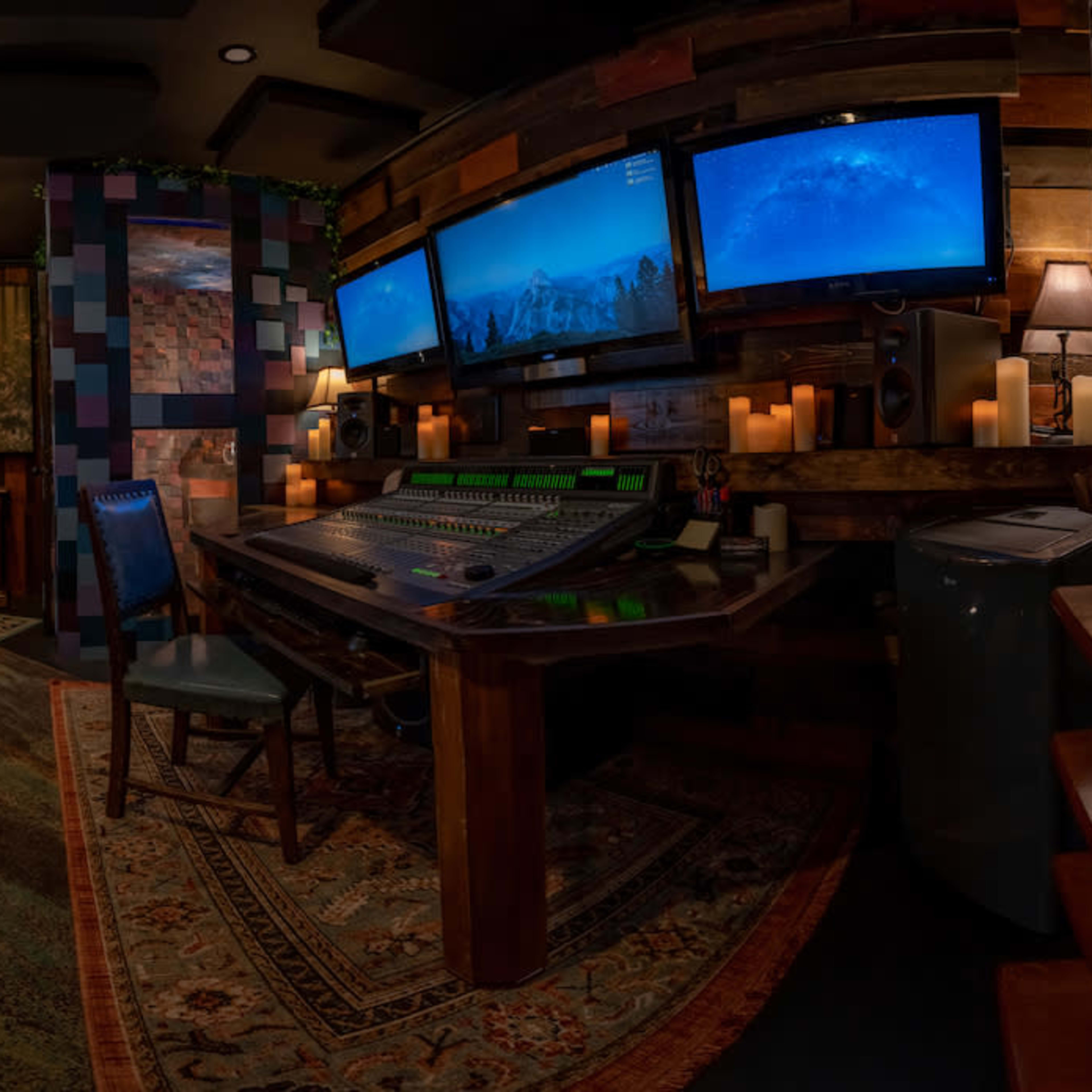 A cozy audio recording studio with a mixing console, multiple monitors displaying ocean scenes, comfortable seating, and ambient lighting.
