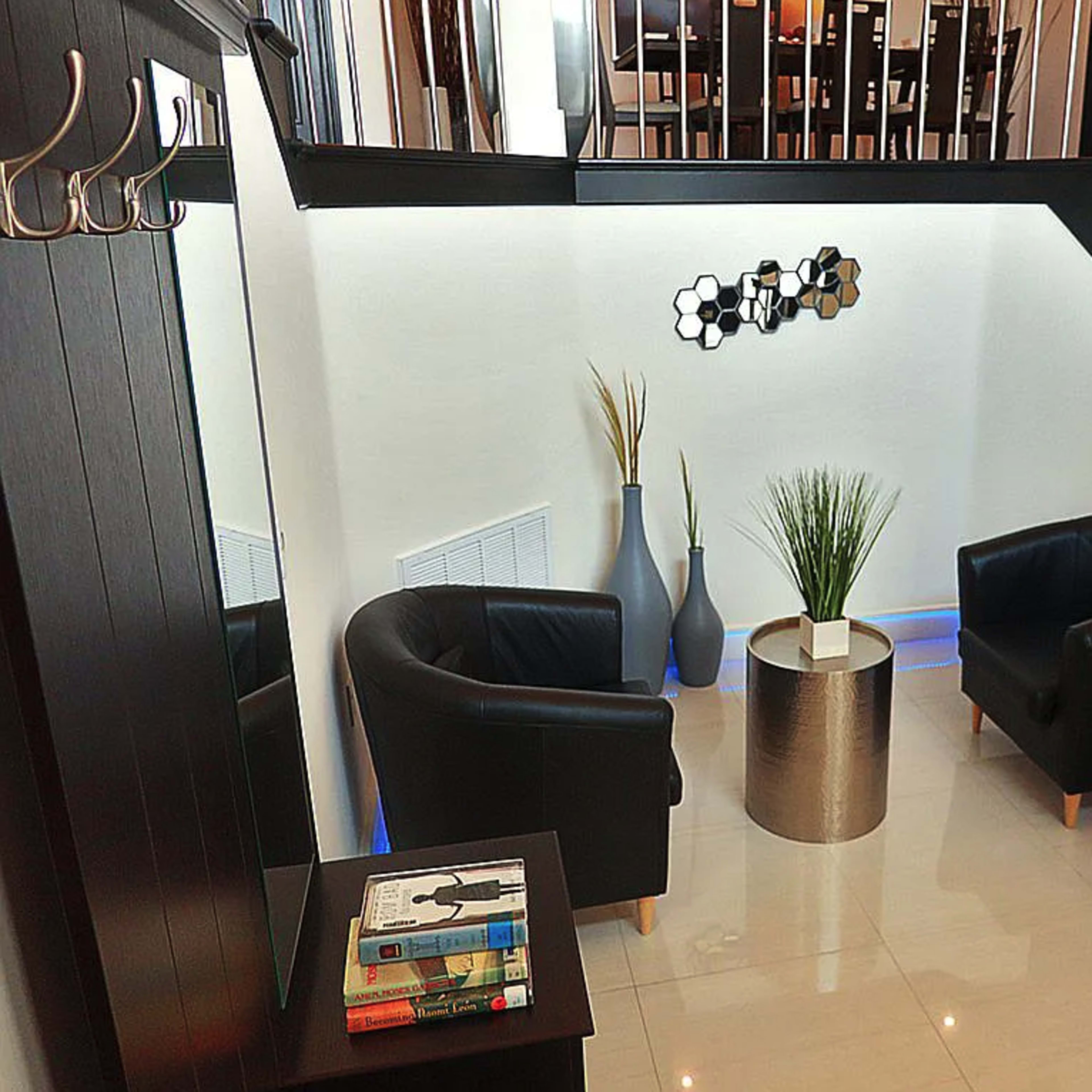 A modern entryway with black leather chairs, a round table, decorative vases, and a spiral staircase, illuminated by soft blue lighting along the base.