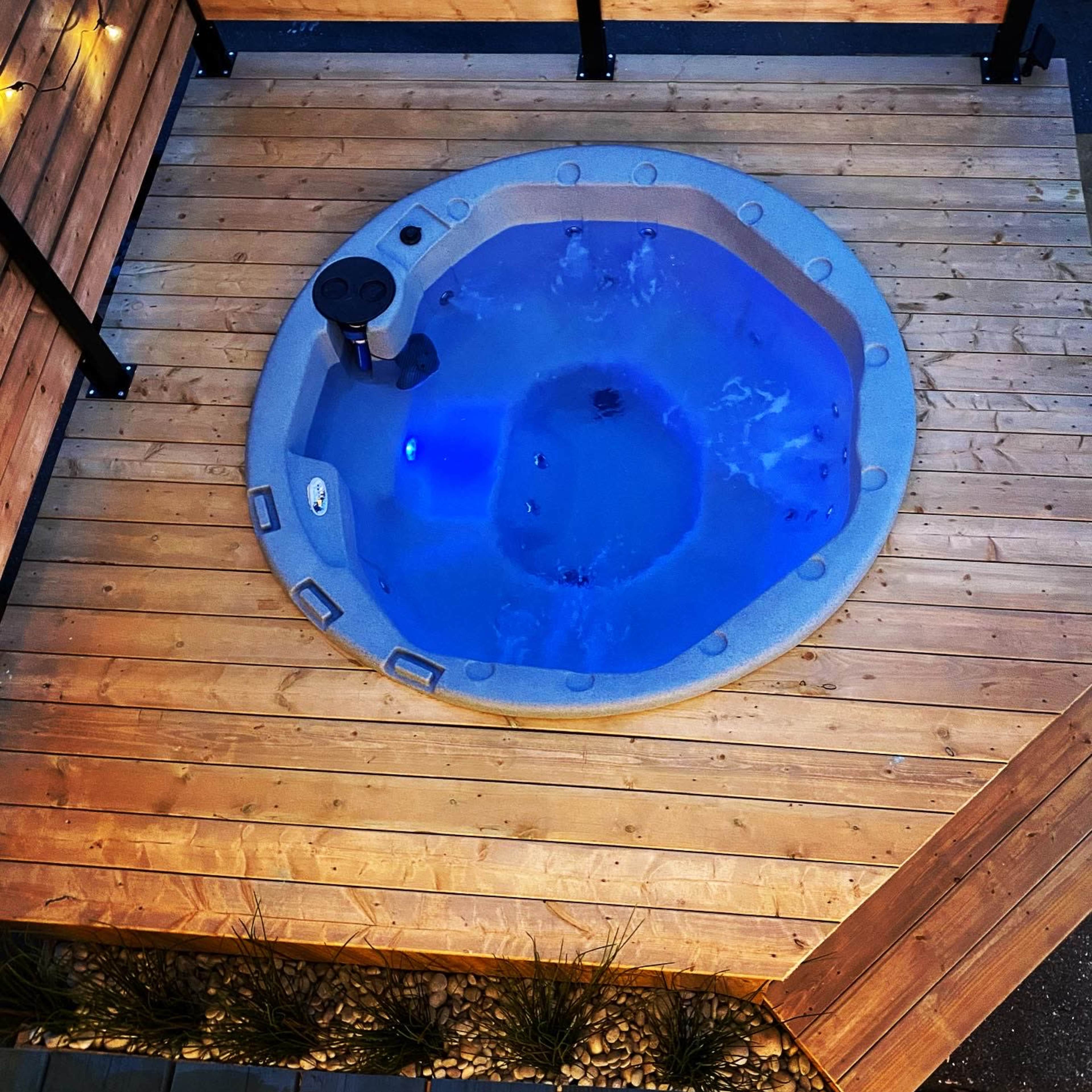 A circular hot tub with blue water, situated on a wooden deck surrounded by glowing string lights.