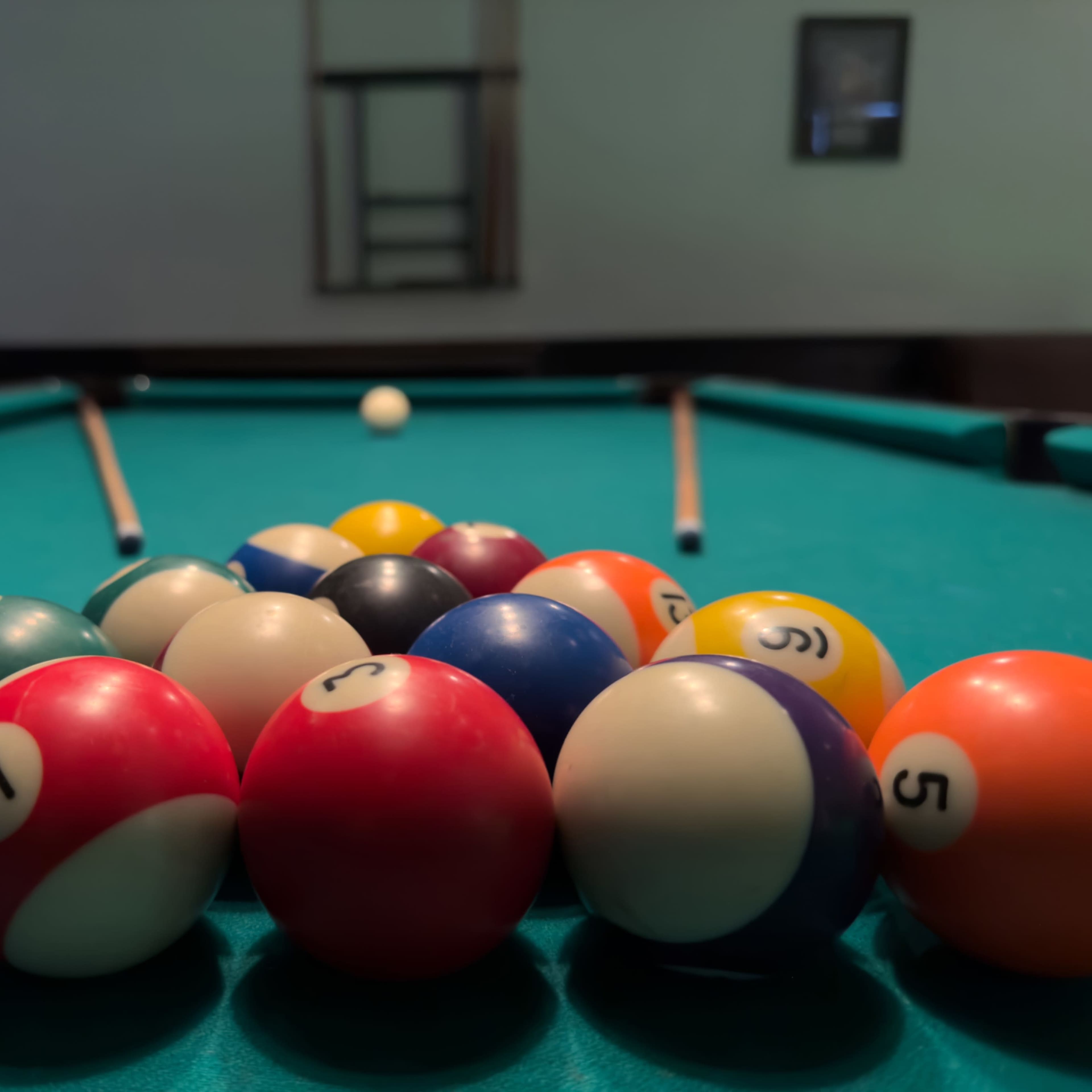 A cluster of colorful billiard balls is arranged on a green pool table, with cues visible in the background.
