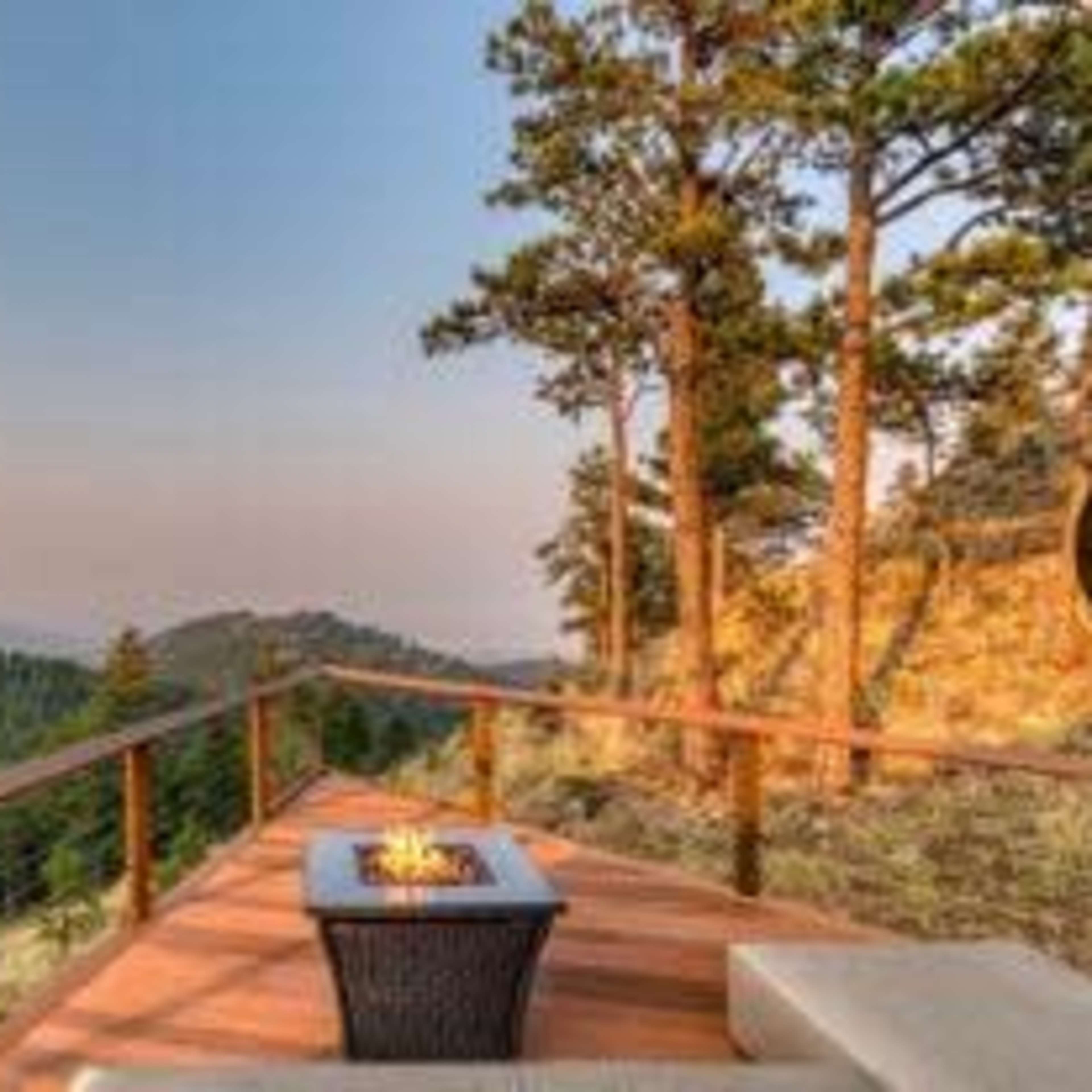 A wooden deck with seating overlooks a mountainous landscape and features a fire pit at its center.