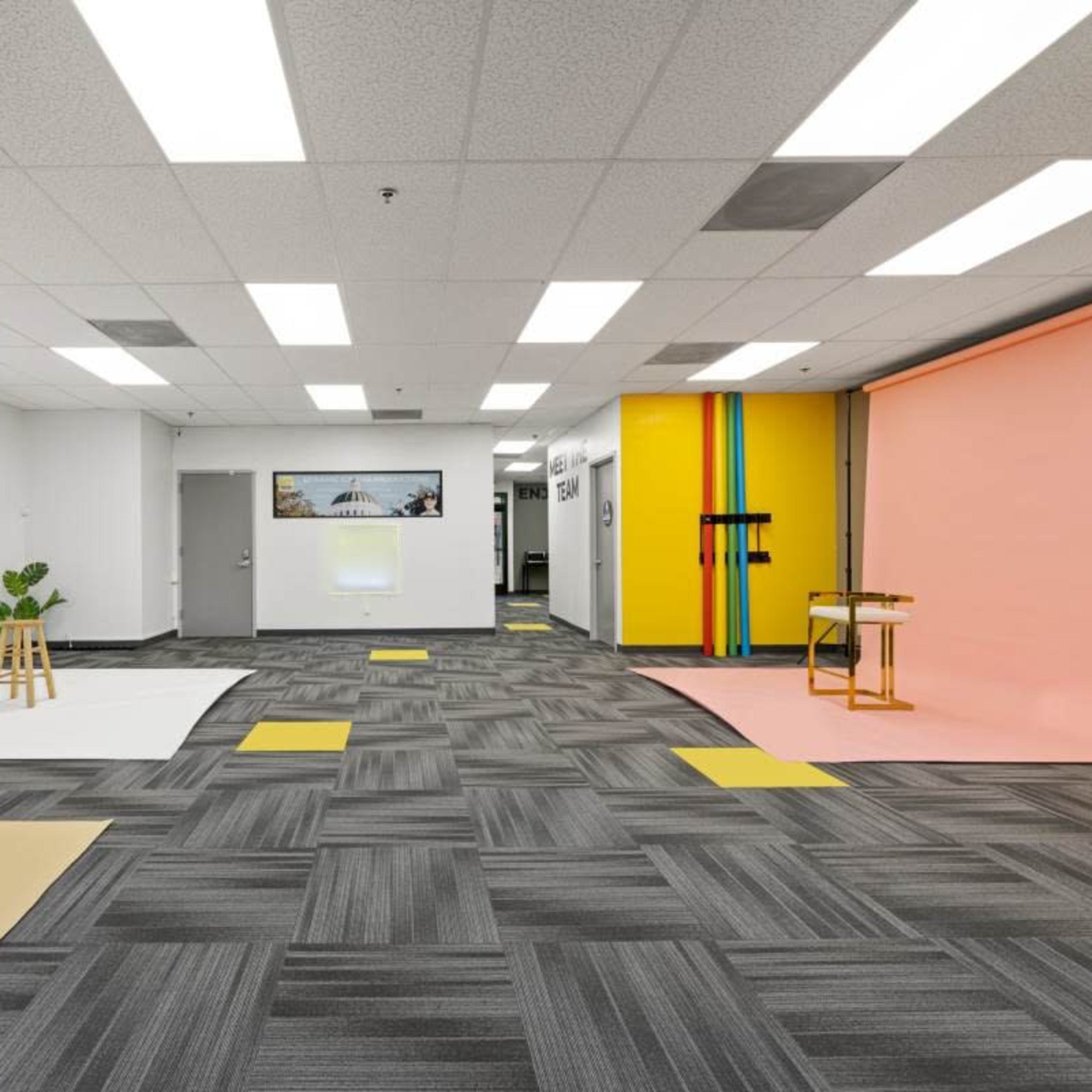 A spacious studio with various backdrops, including a white, pink, and yellow wall, along with modern flooring and lighting fixtures.