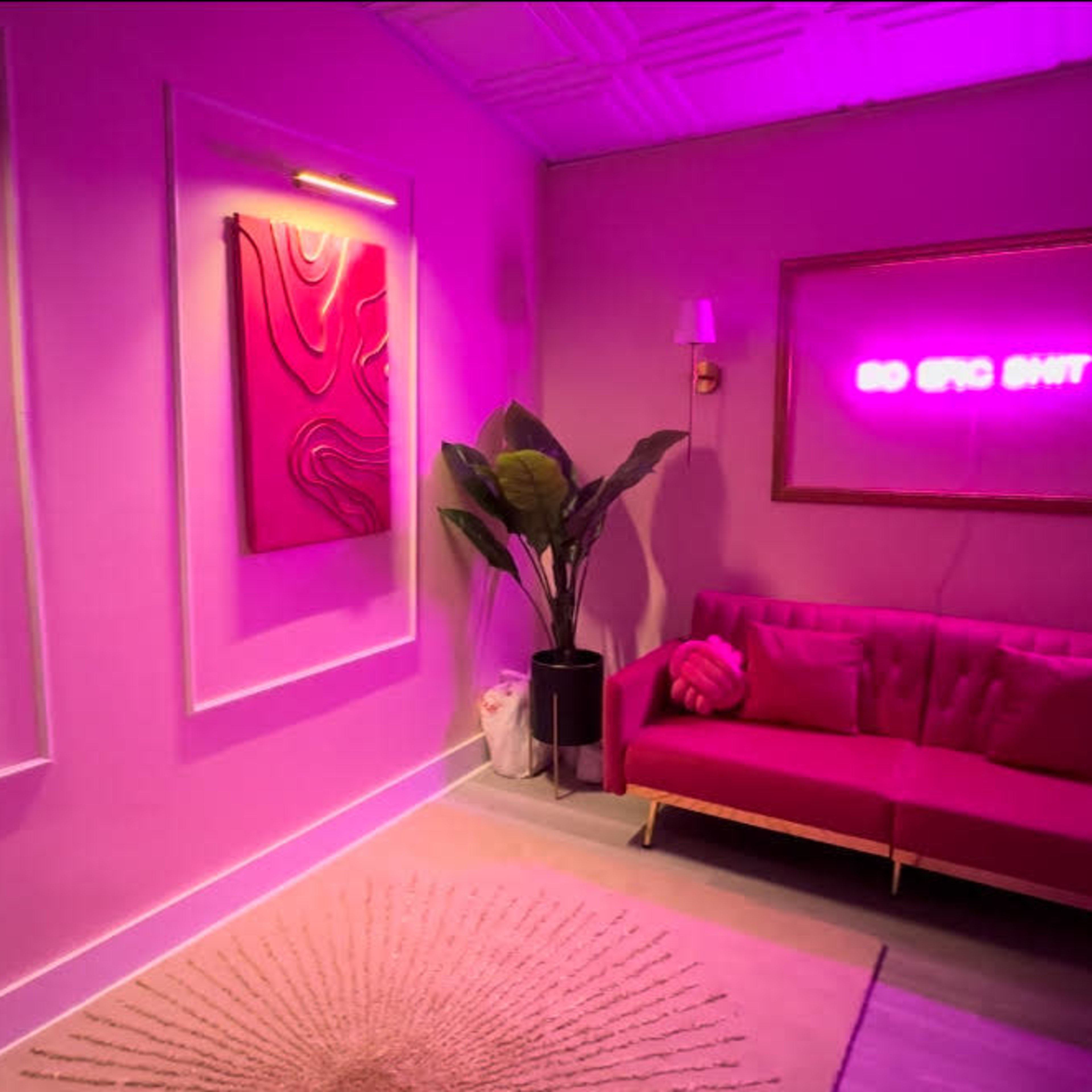 A modern room with pink wall art, a pink sofa, and a neon sign that reads "GO EPIC SHIT" illuminated against a pastel background.