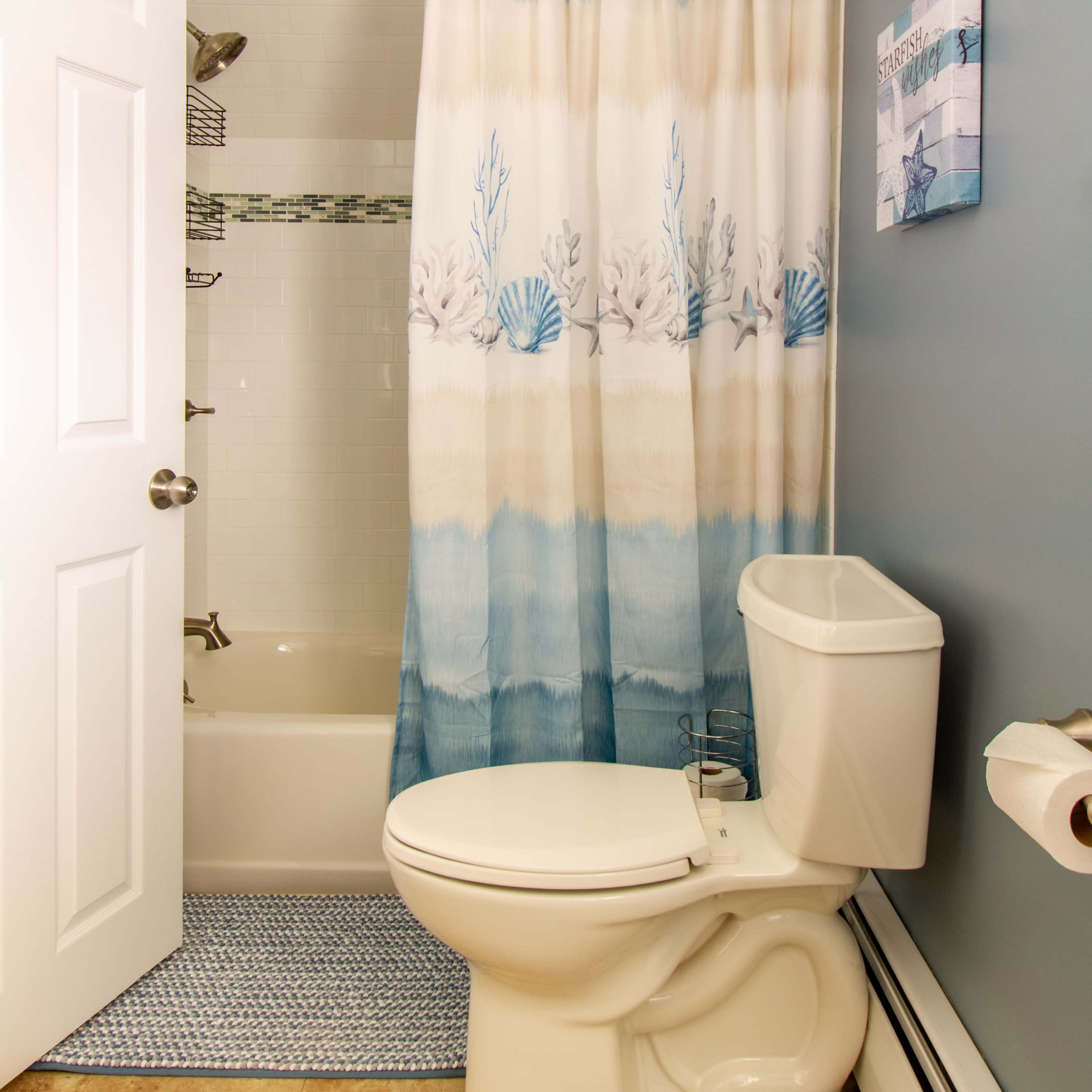 A bathroom with a shower curtain featuring a sea-themed design, a toilet, and a blue wall.