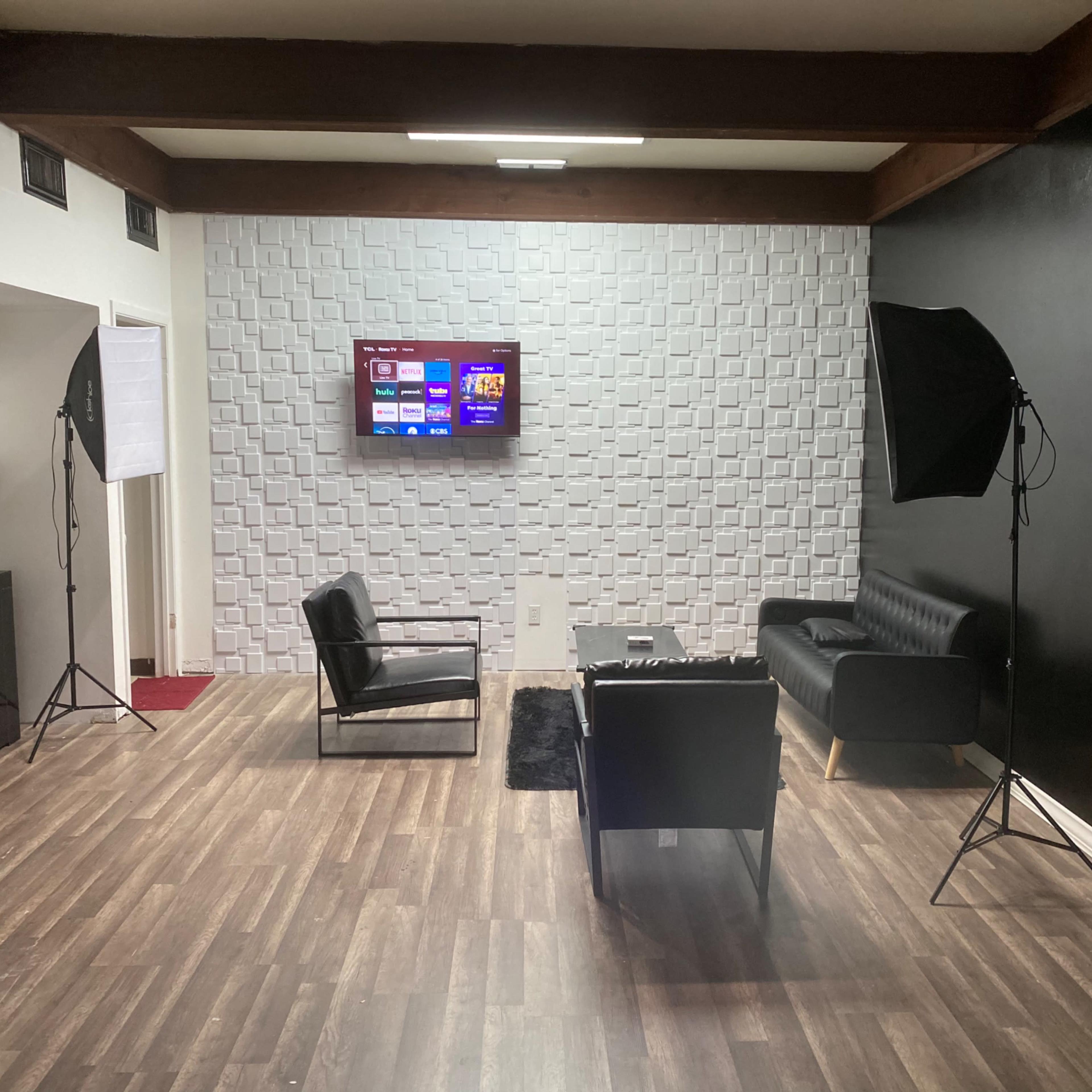 A modern sitting area with two chairs, a sofa, a wall-mounted television, and two lighting setups on either side.