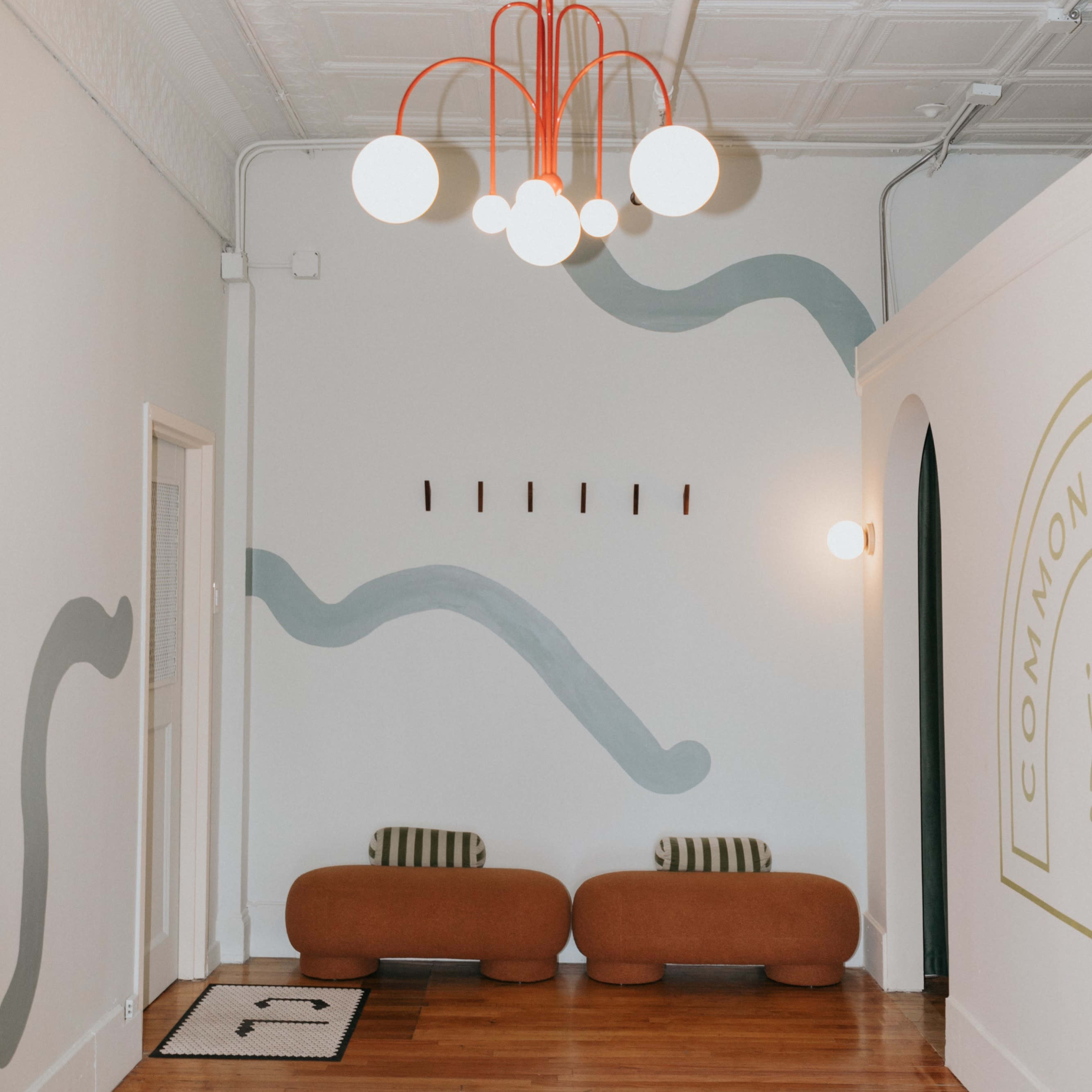 A room with two brown benches, a stylish chandelier with white globes and red accents, and patterned walls featuring wavy green designs.