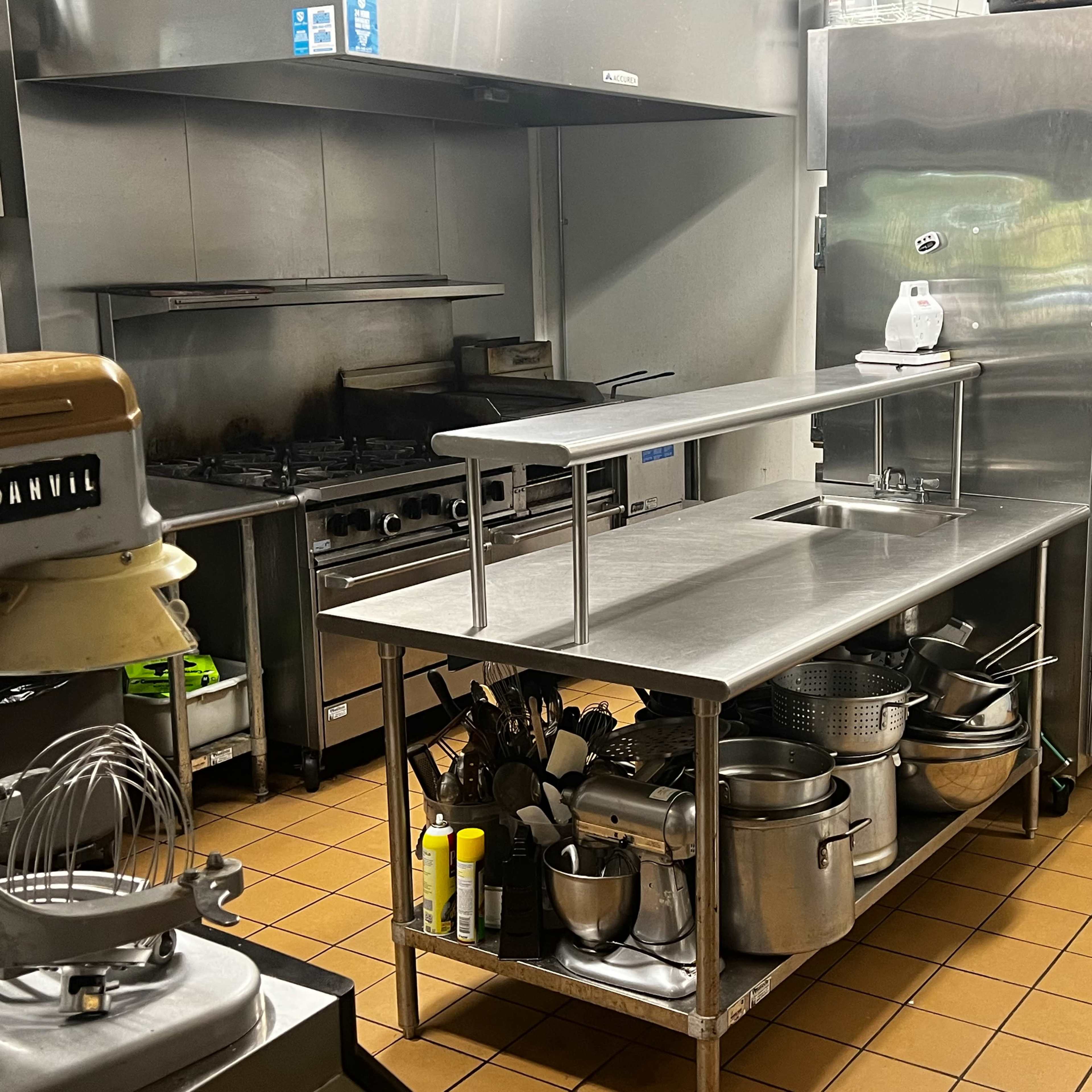 A commercial kitchen with a stainless steel prep table, various pots and utensils organized nearby, and stainless steel appliances in the background.