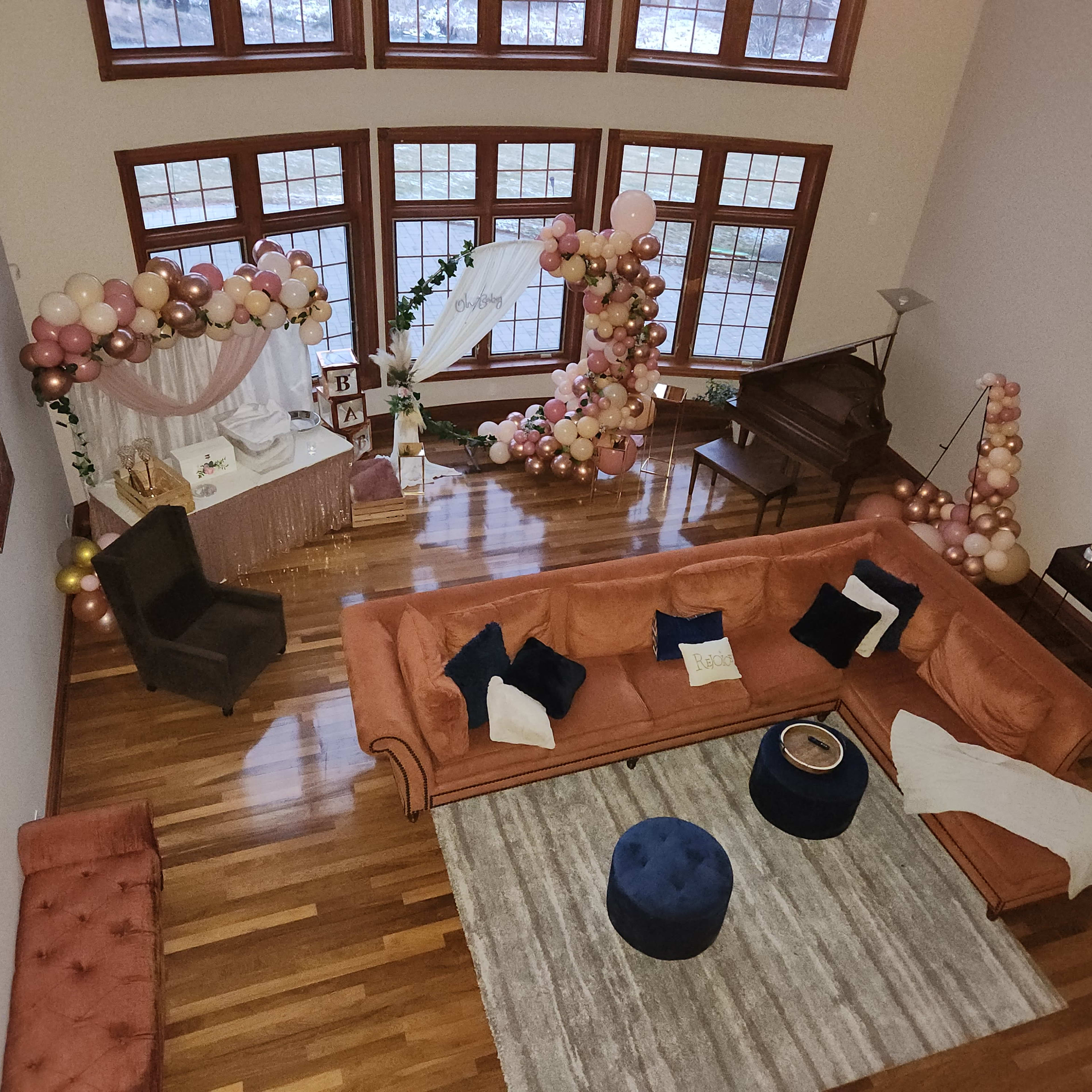A spacious living room with a large orange sectional sofa, a round blue ottoman, and a decorated corner featuring a balloon arch and a table set up for an event.
