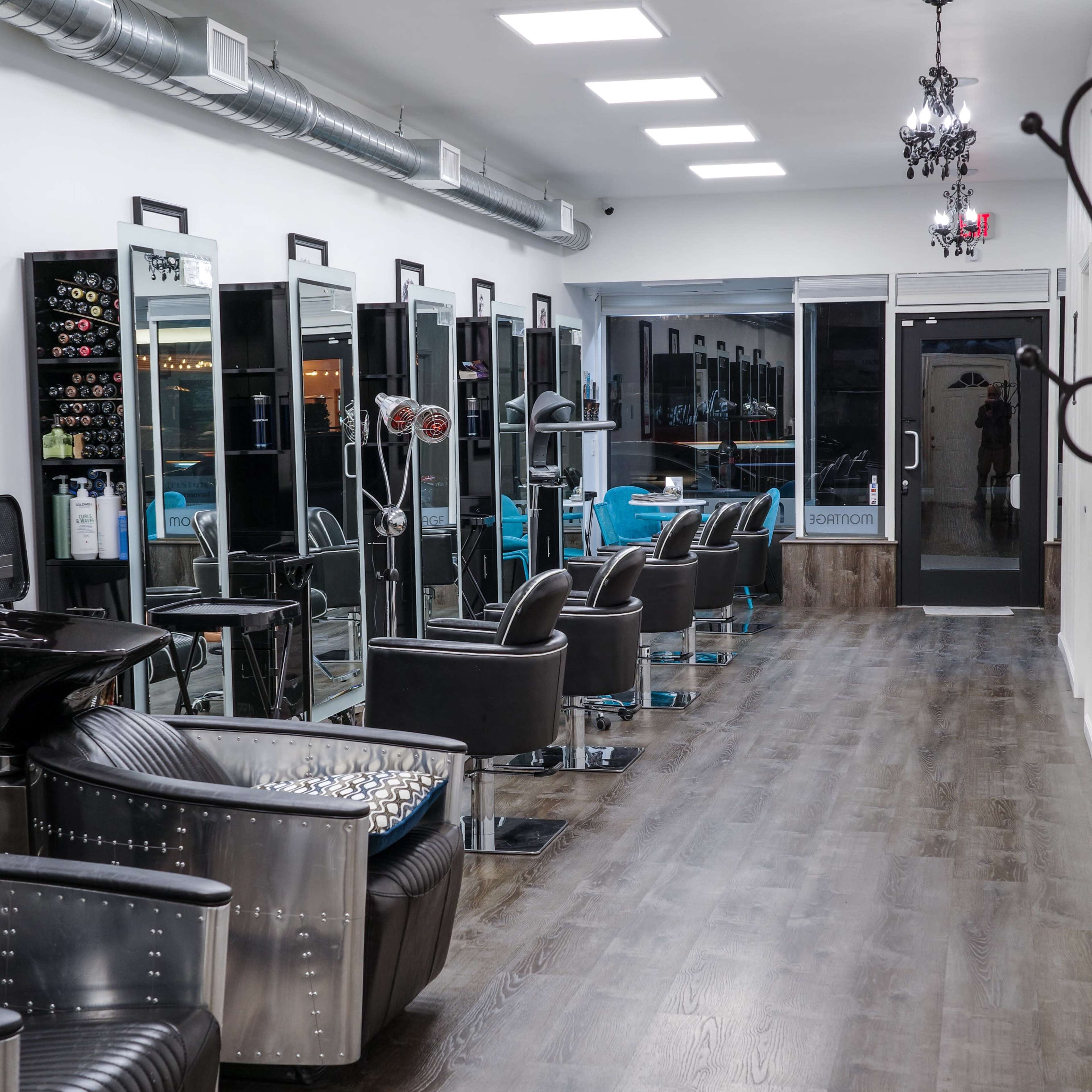 A modern hair salon with styling stations, mirrors, and black chairs arranged along a well-lit corridor.