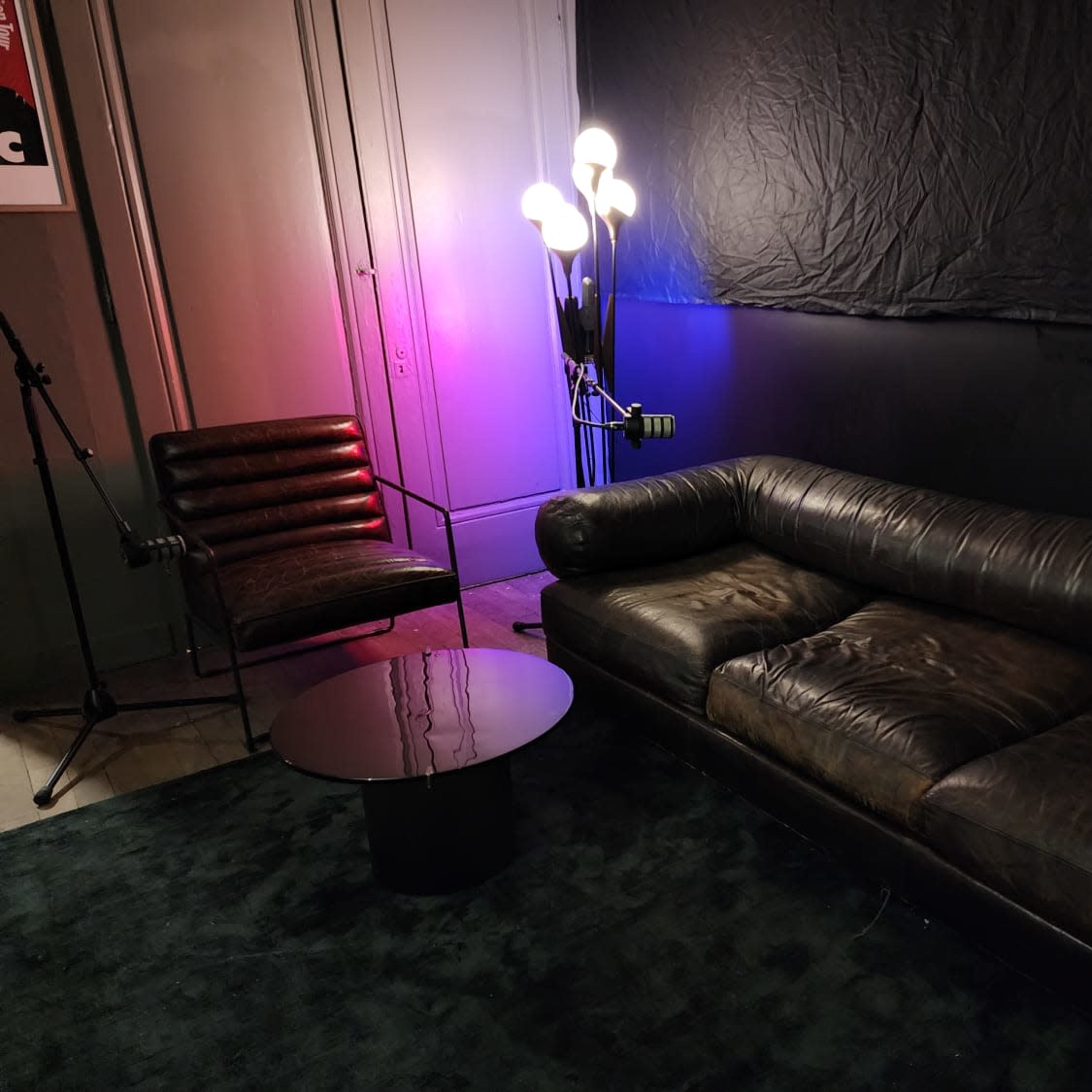 The scene features a dark room with a leather sofa, a modern chair, a round table, and a lamp with multiple light bulbs illuminating the space.